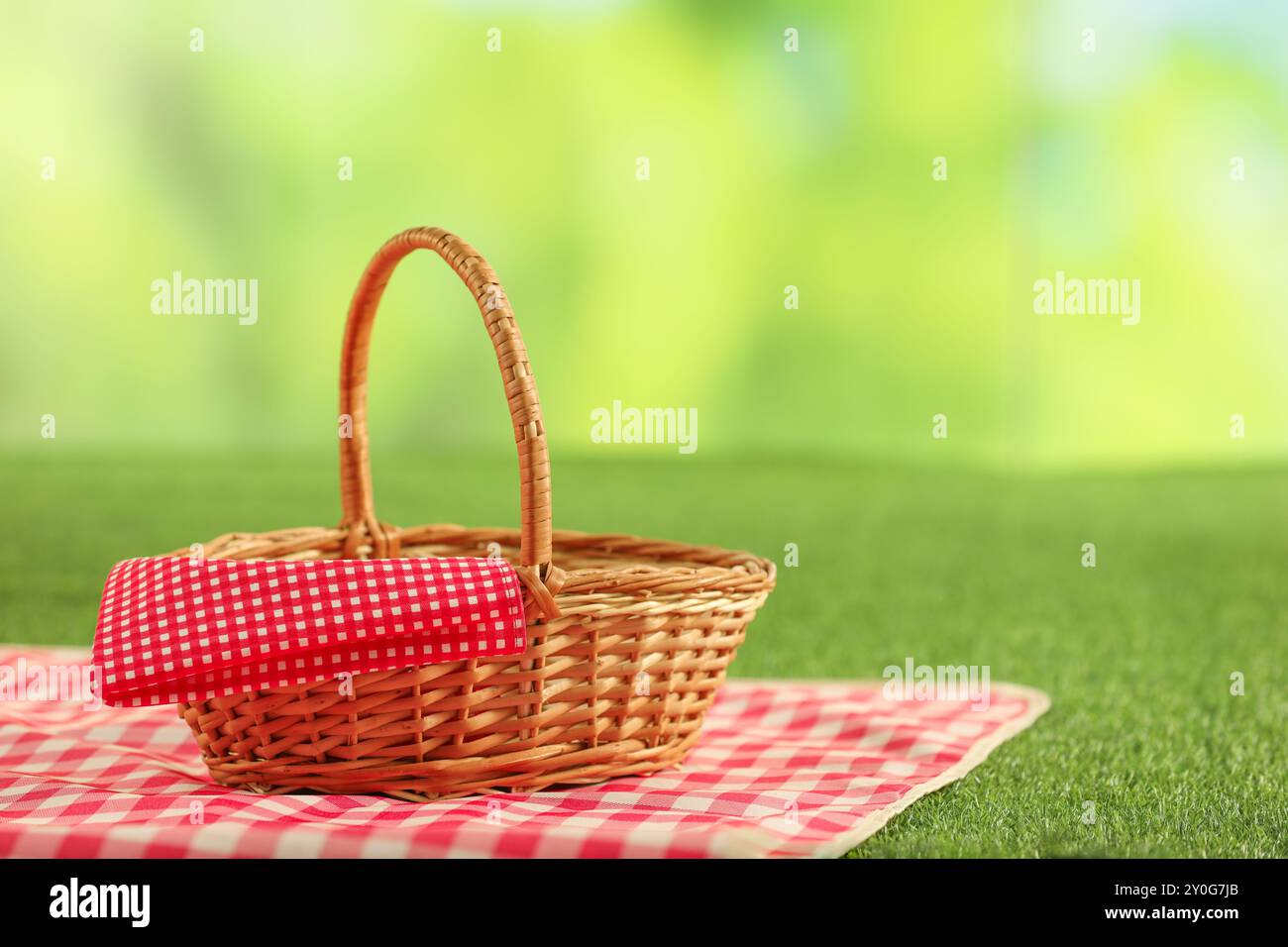 One picnic wicker basket with checkered napkin and blanket on grass ...