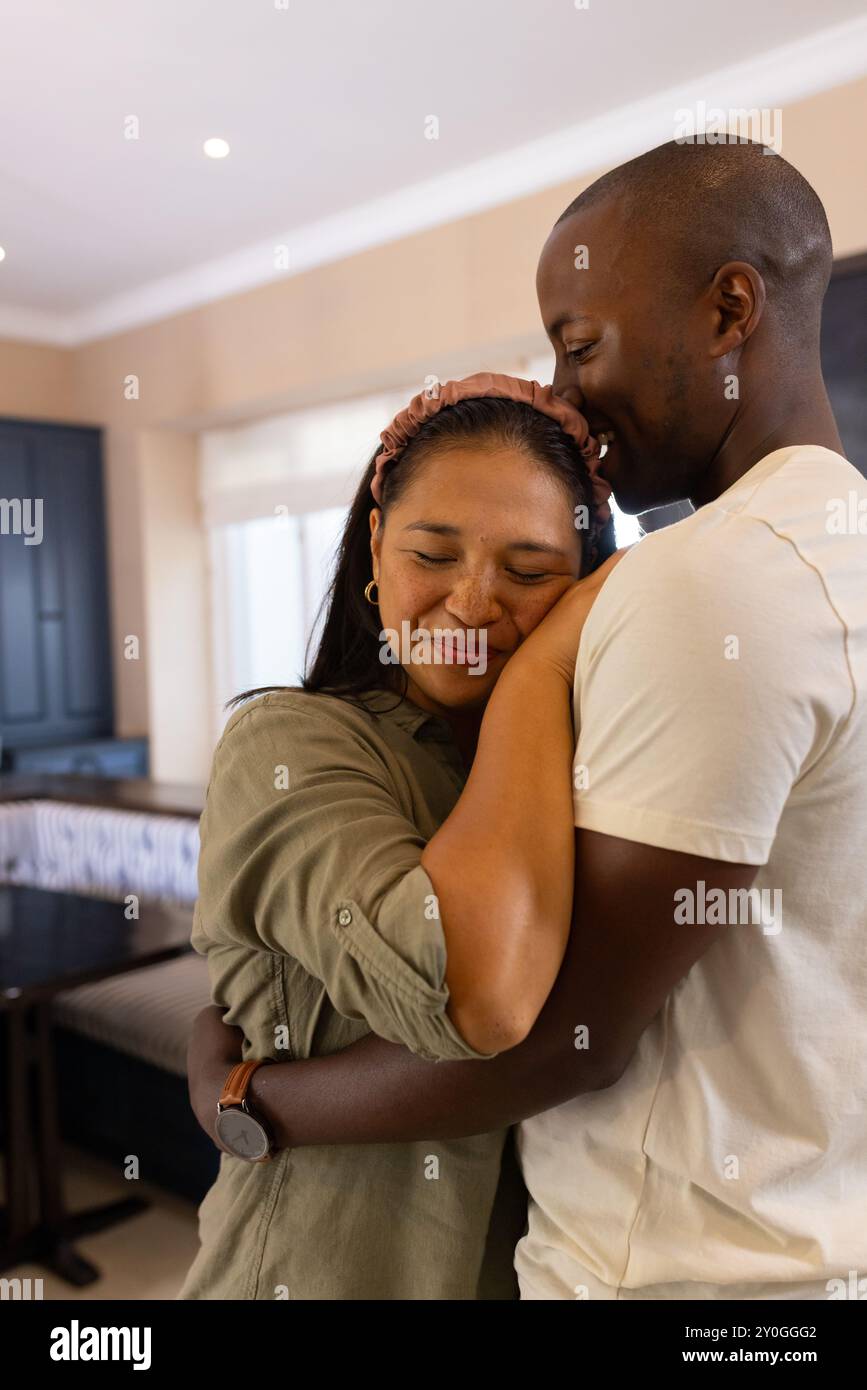 Embracing warmly, multiracial couple enjoying tender moment together at home Stock Photo