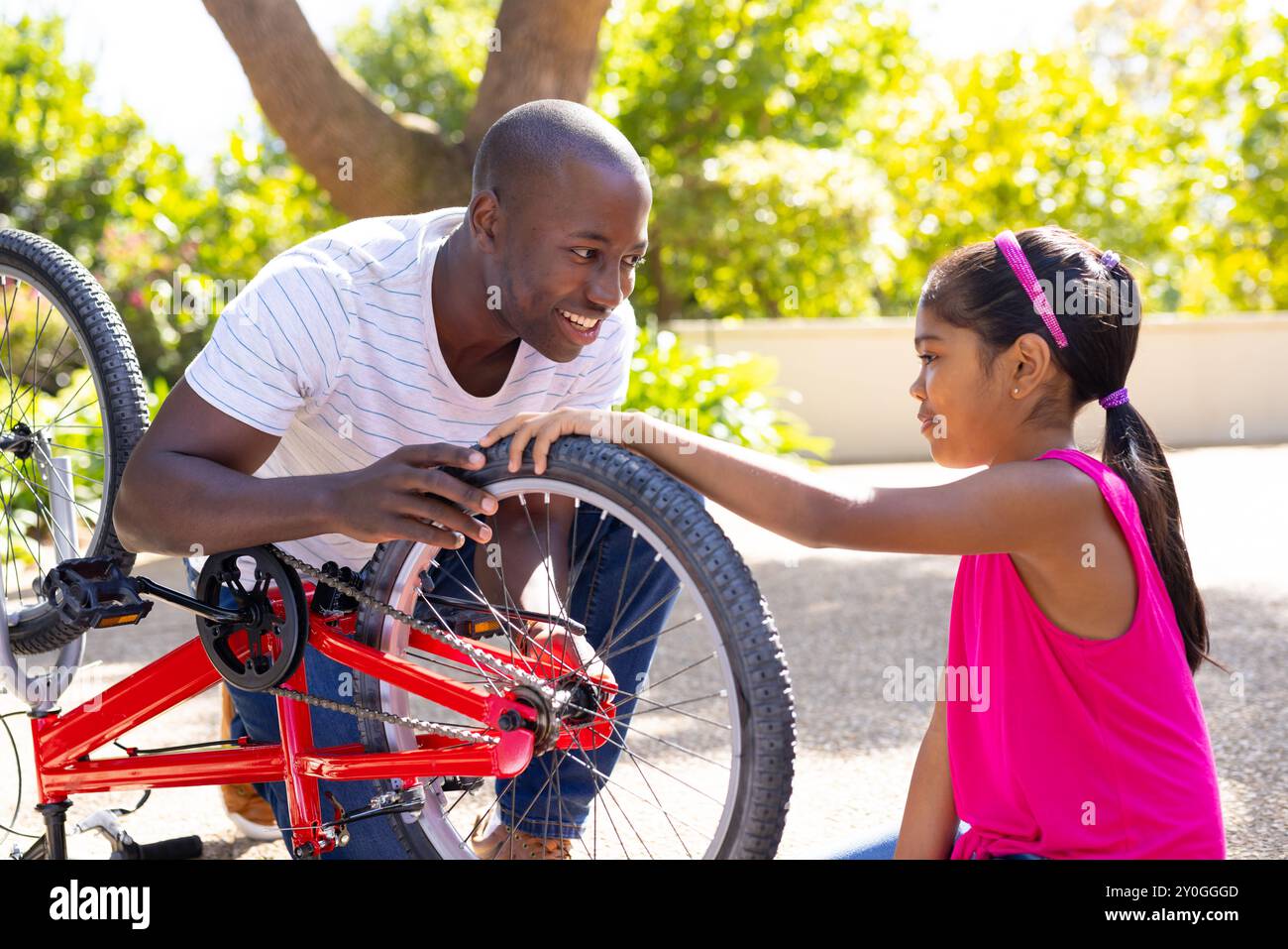 Fixing bicycle, father teaching daughter how to repair bike in outdoor setting Stock Photo