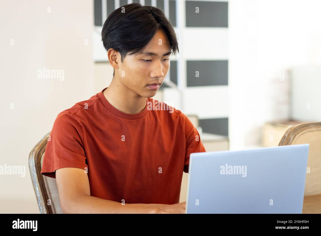 Working on laptop, young asian man concentrating on task in modern office setting Stock Photo