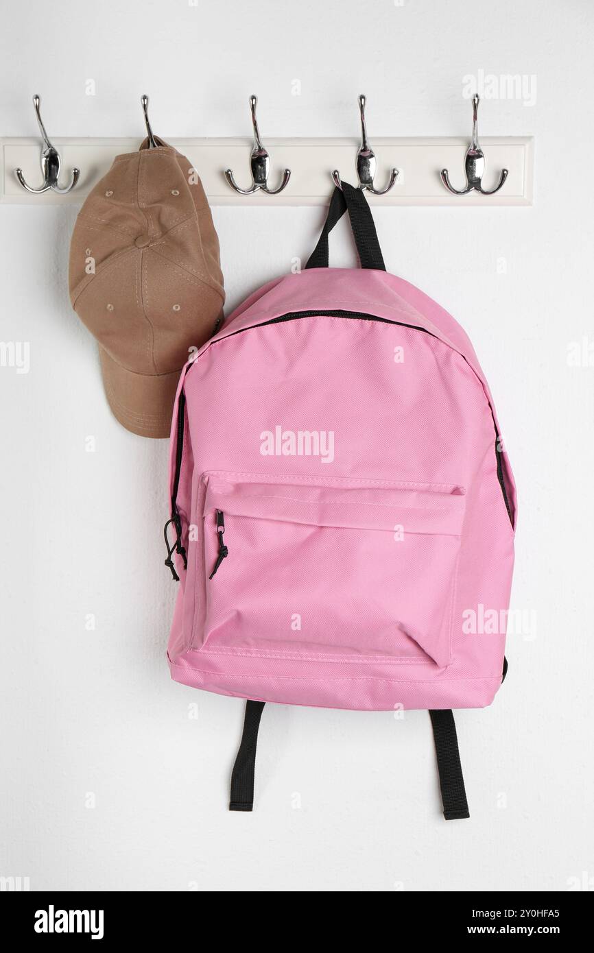 Pink backpack and cap hanging on white wall Stock Photo