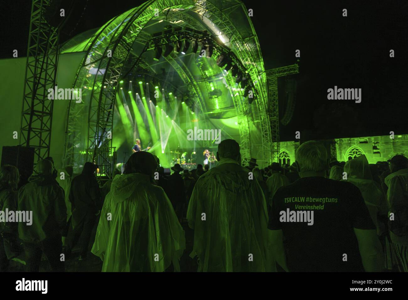 People in rain ponchos and a T-shirt in the crowd at a night concert with green stage lighting, Klostersommer, Calw Hirsau, Black Forest, Germany, Eur Stock Photo