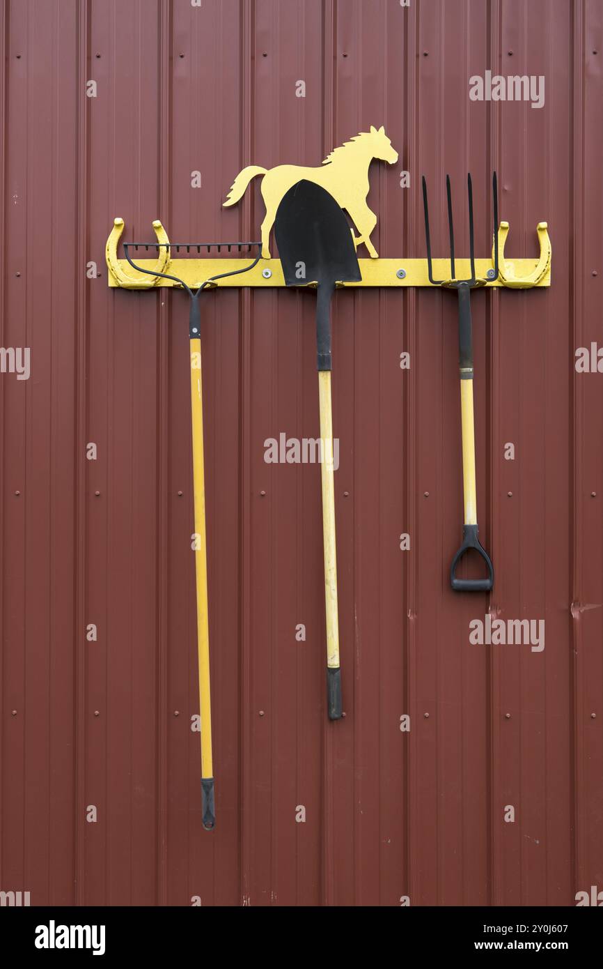 A concept photo of a rake, a shovel, and a pitchfork hanging on a rack ...