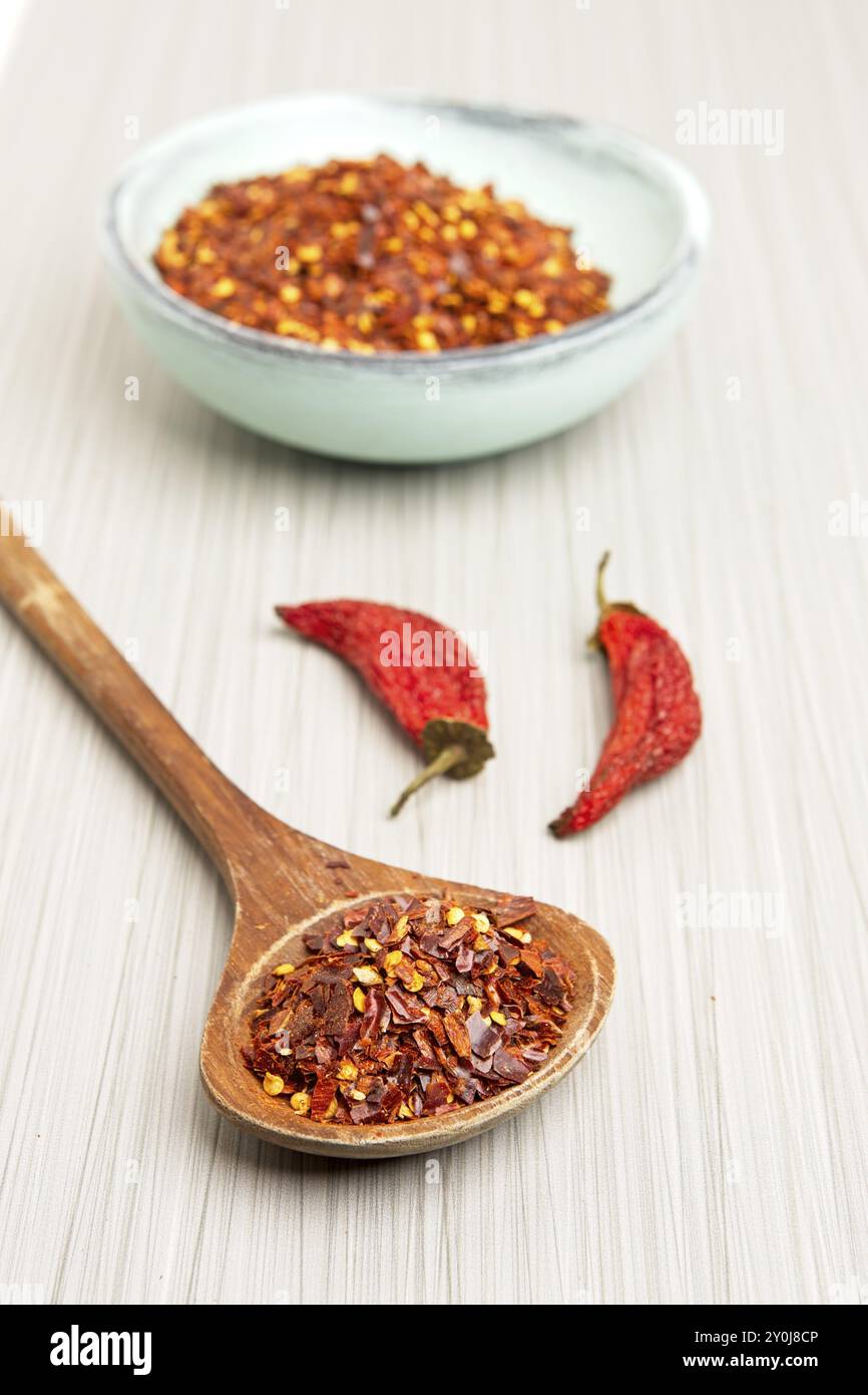 Studio photo of red pepper flakes on a wooden spoon with a blue wooden bowl of pepper powder and whole red peppers Stock Photo