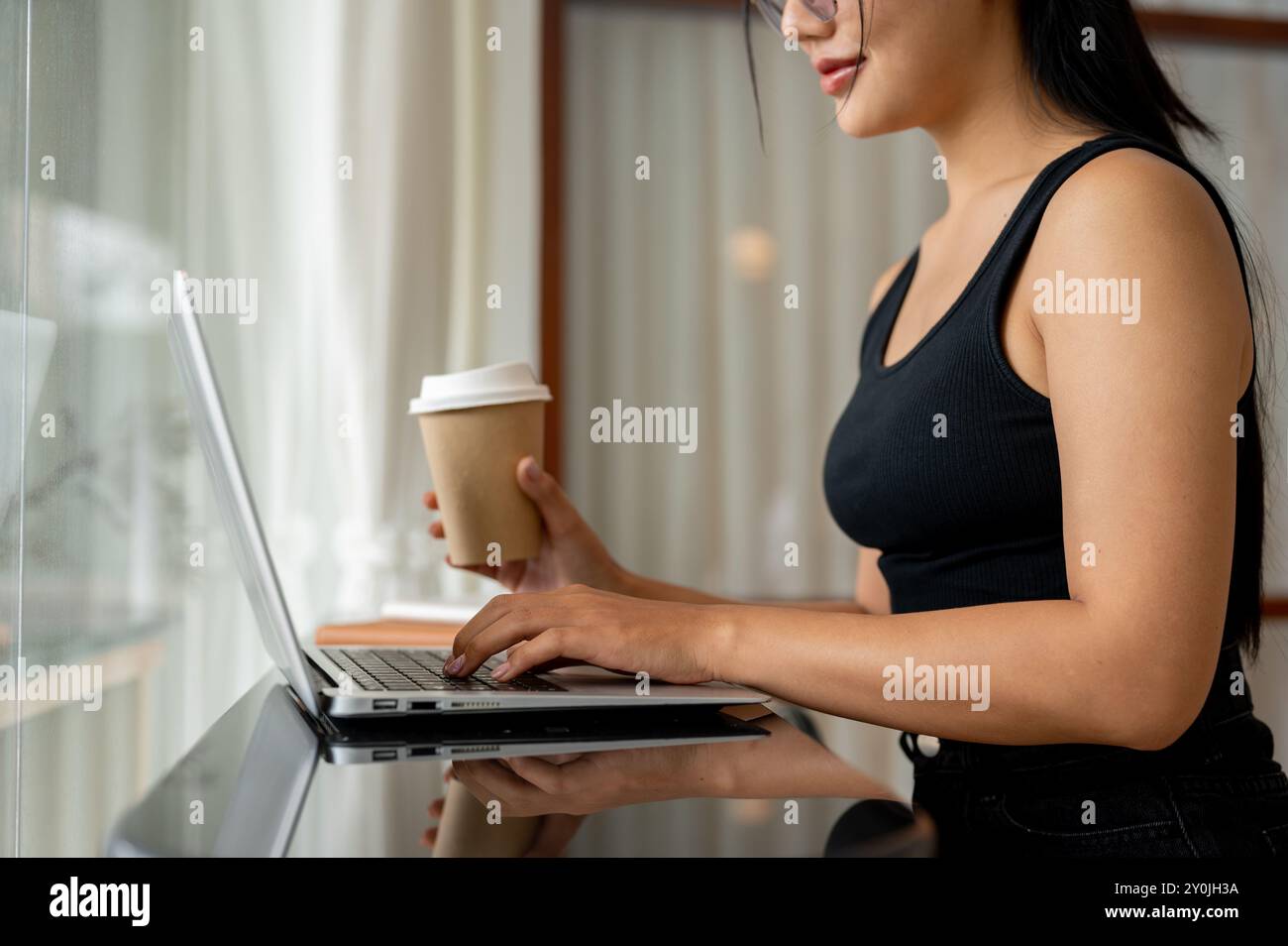 A cropped side view of an attractive Asian woman working remotely from ...