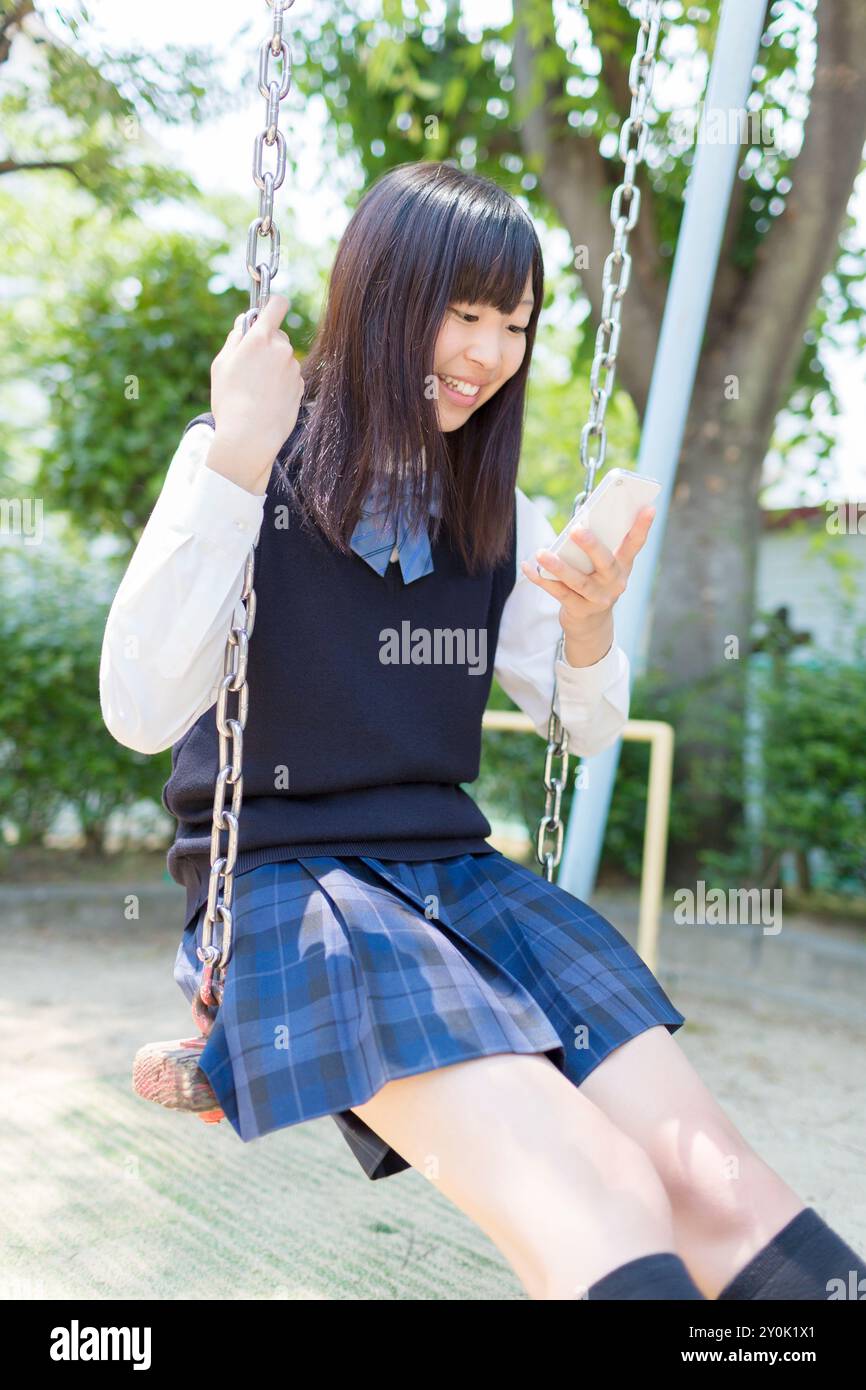 School girl riding on a swing while looking at a cell phone Stock Photo