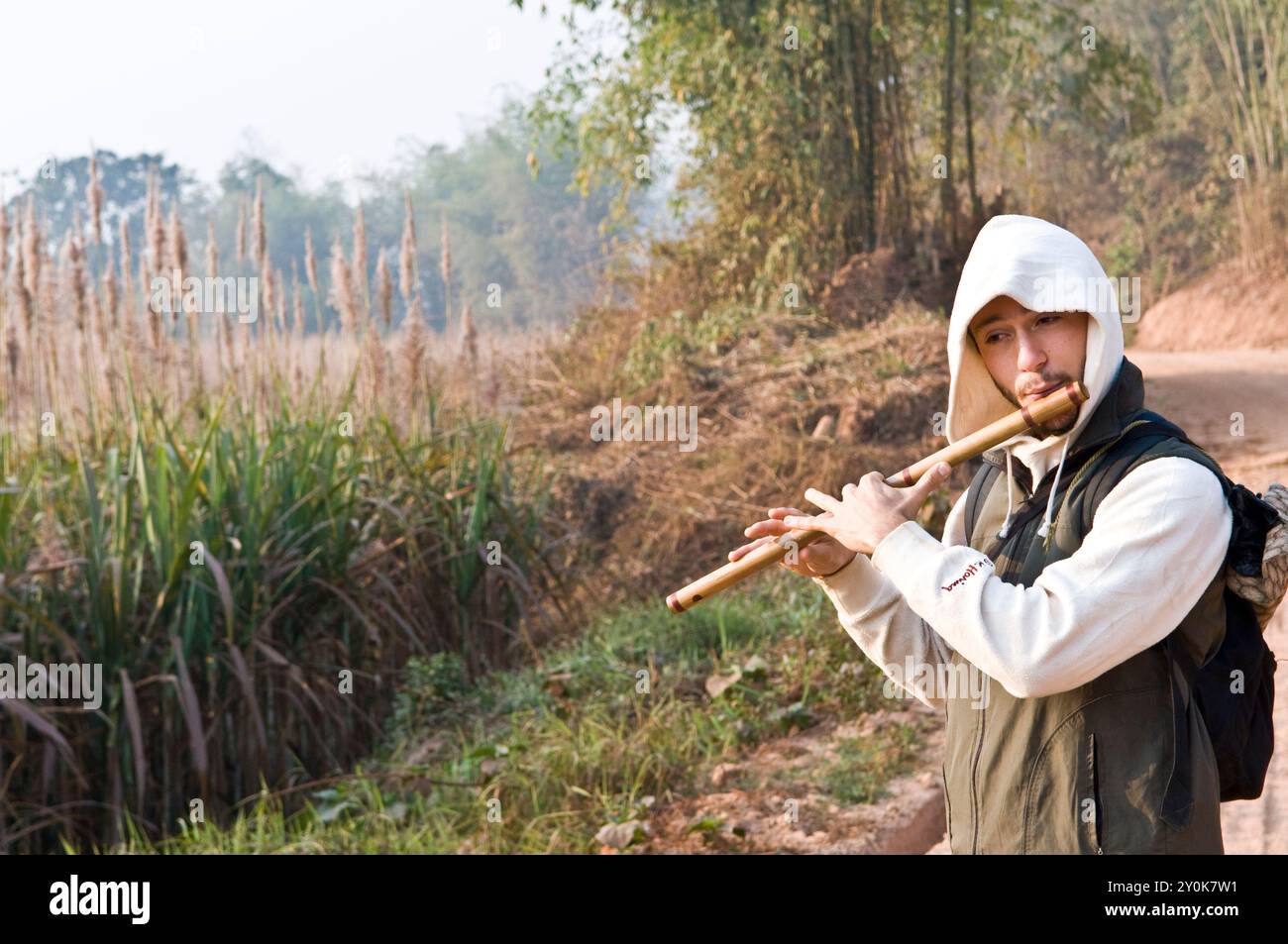 A traveler playing his Indian classical flute on a small path between the sugarcane fields. Stock Photo