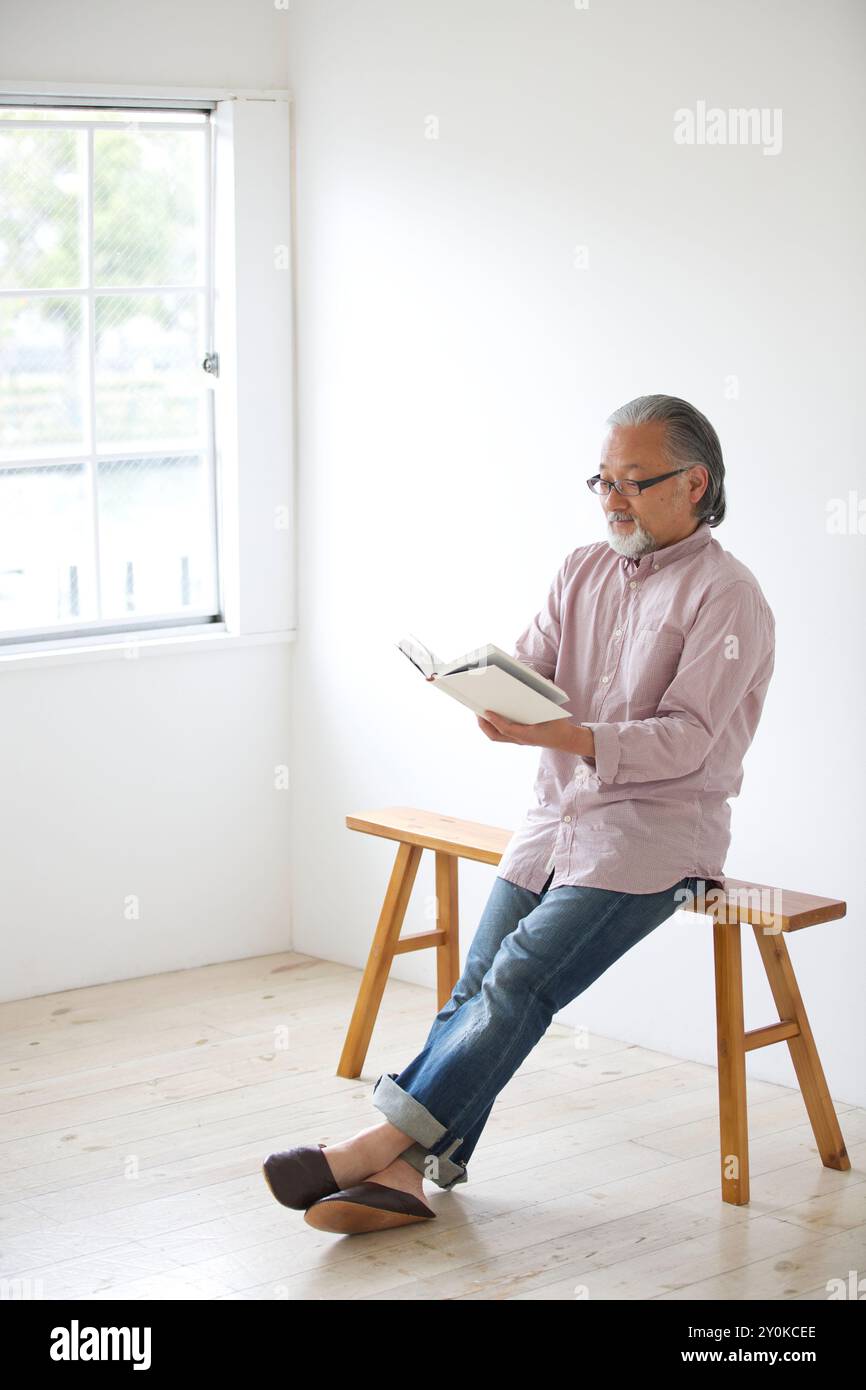 Senior man sitting on a bench and reading a book Stock Photo - Alamy