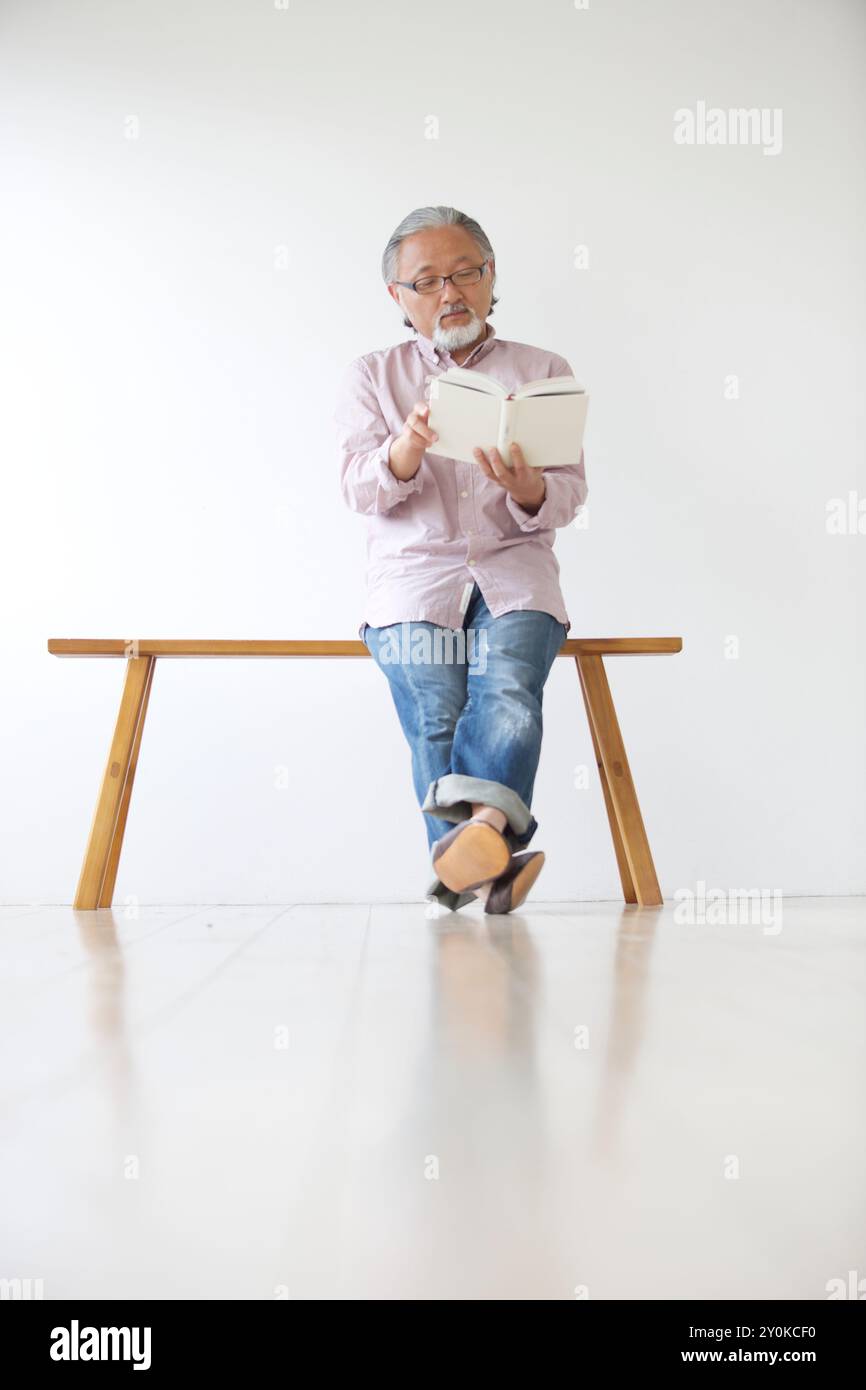 Senior man sitting on a bench and reading a book Stock Photo - Alamy