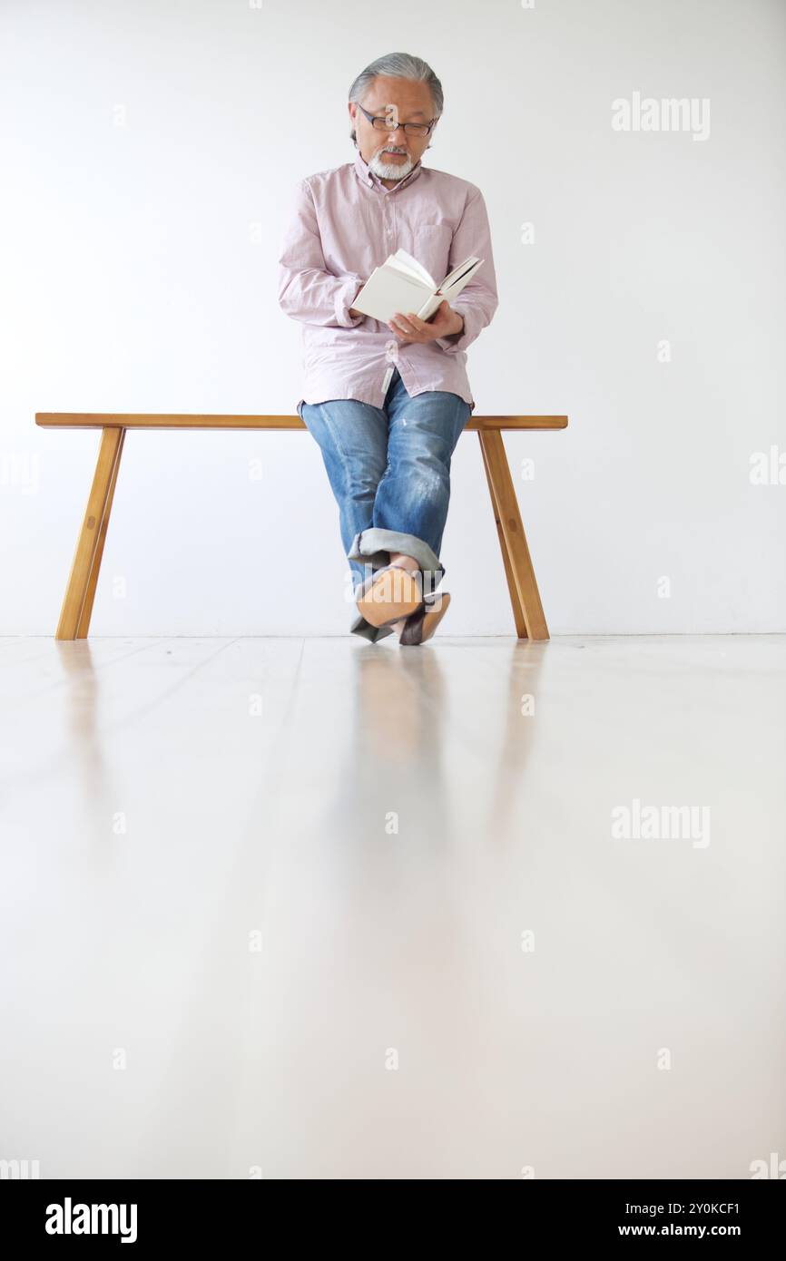 Senior man sitting on a bench and reading a book Stock Photo - Alamy