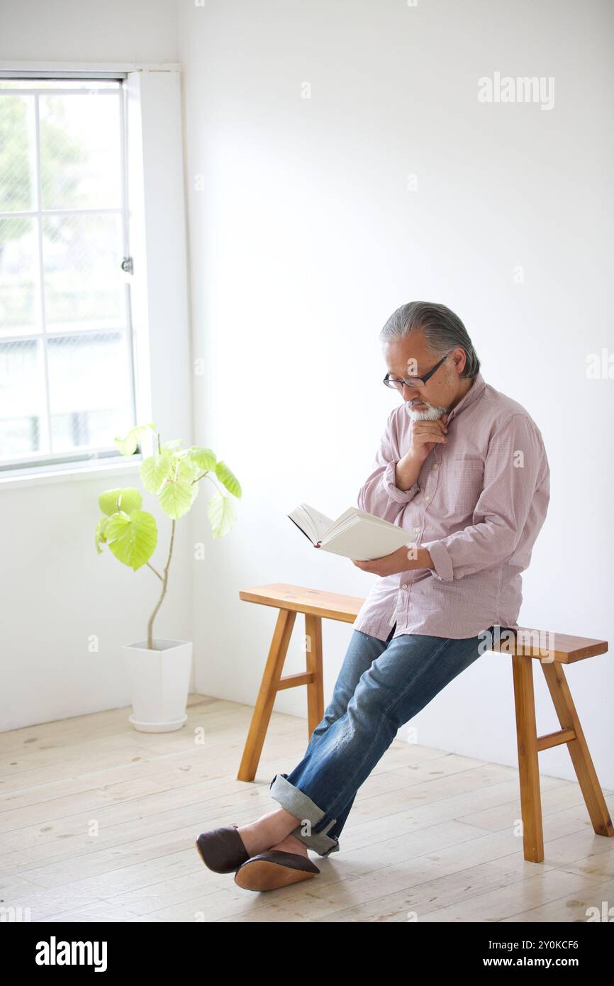 Senior man sitting on a bench and reading a book Stock Photo - Alamy