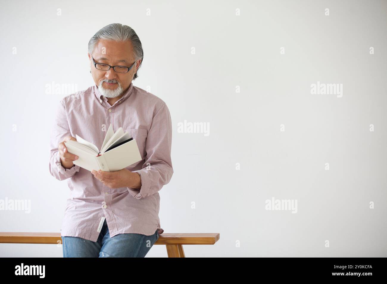 Senior man sitting on a bench and reading a book Stock Photo - Alamy