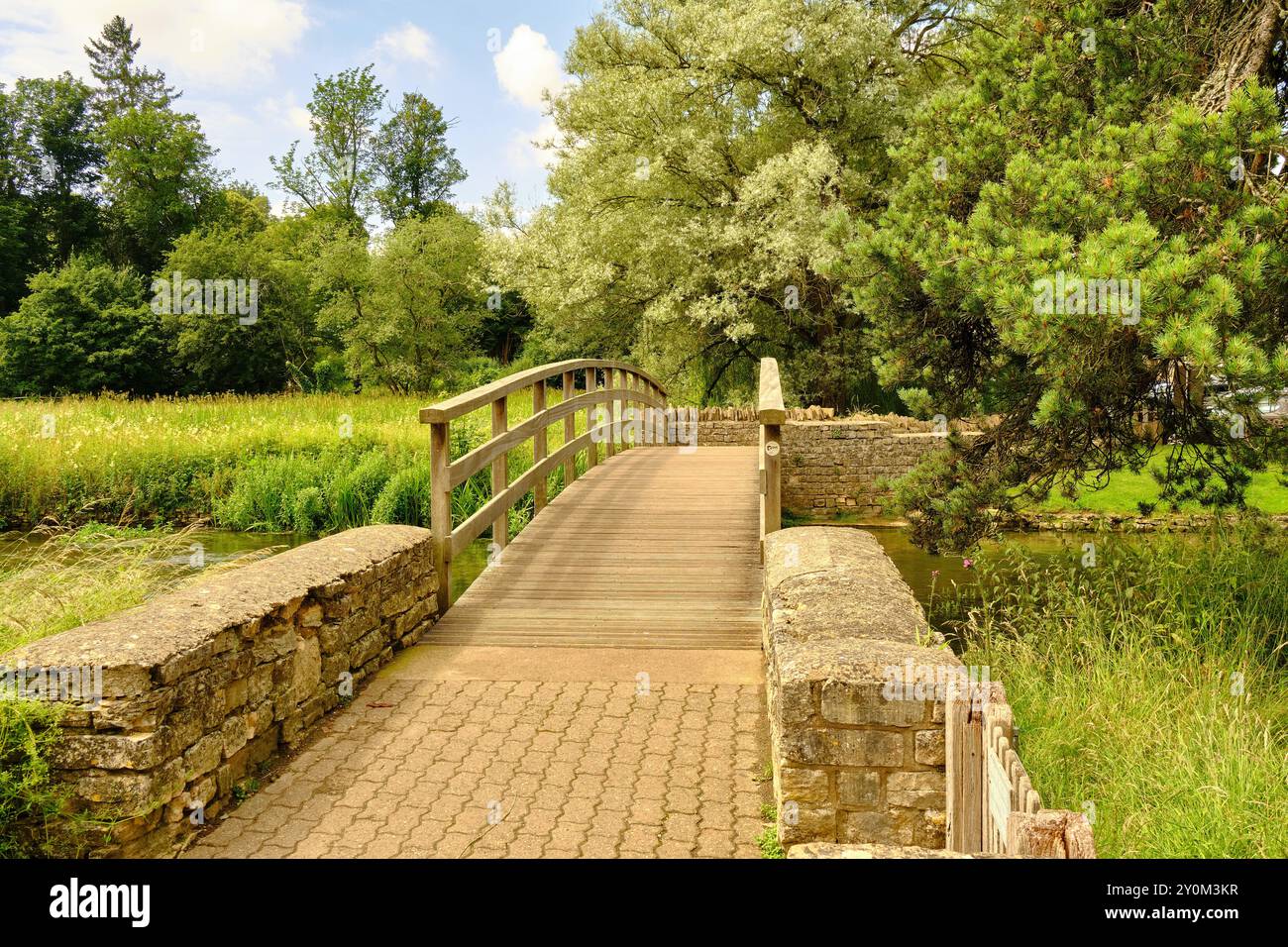 View of a wooden footbridge over the River Coln to the Rack Isle water meadow in the Cotswold village of Bibury, England, UK Stock Photo