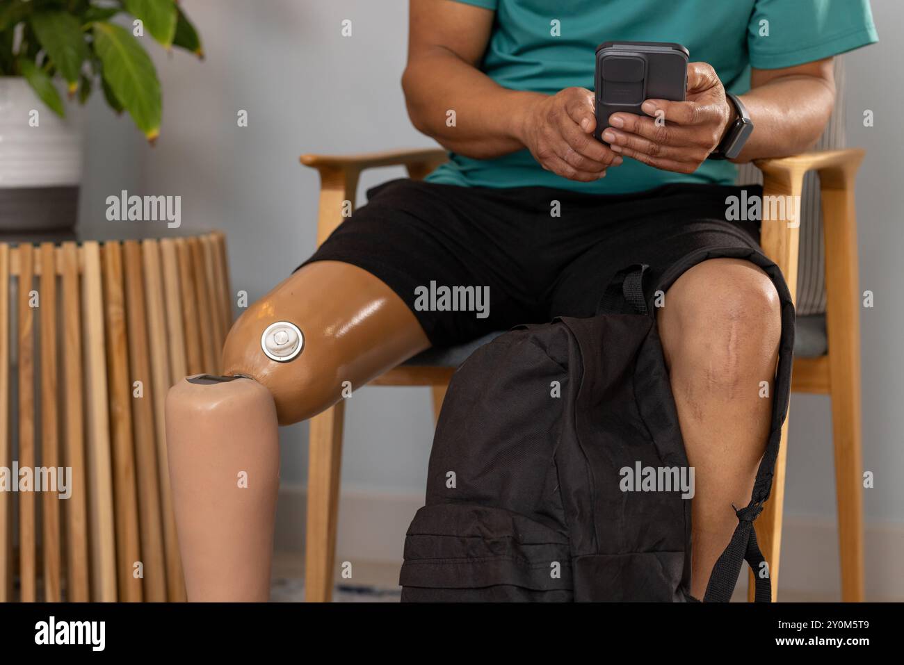 Man with prosthetic leg sitting and using smartphone, backpack on lap Stock Photo
