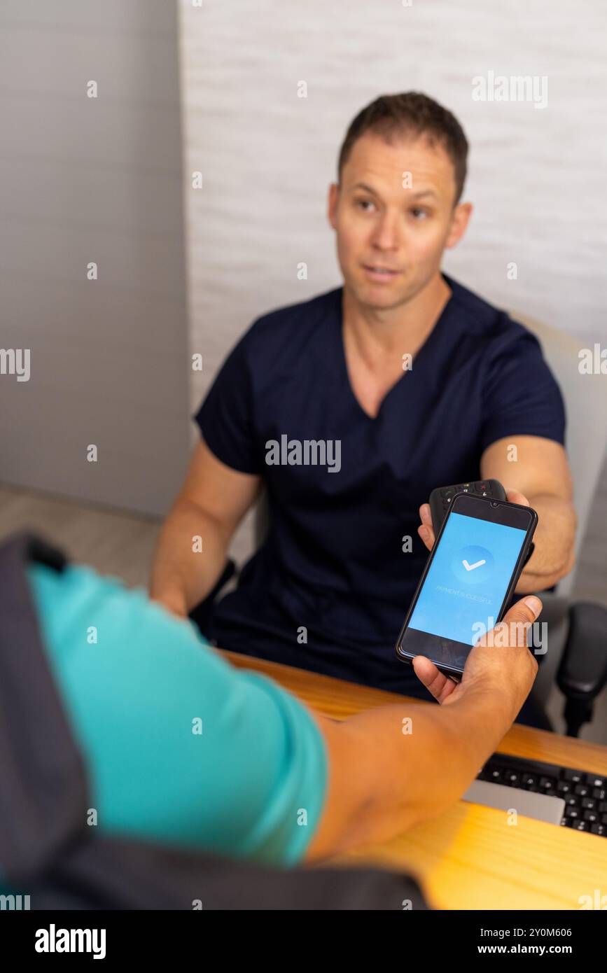 Paying with smartphone, male doctor or healthcare worker in scrubs, patient visiting medical clinic Stock Photo