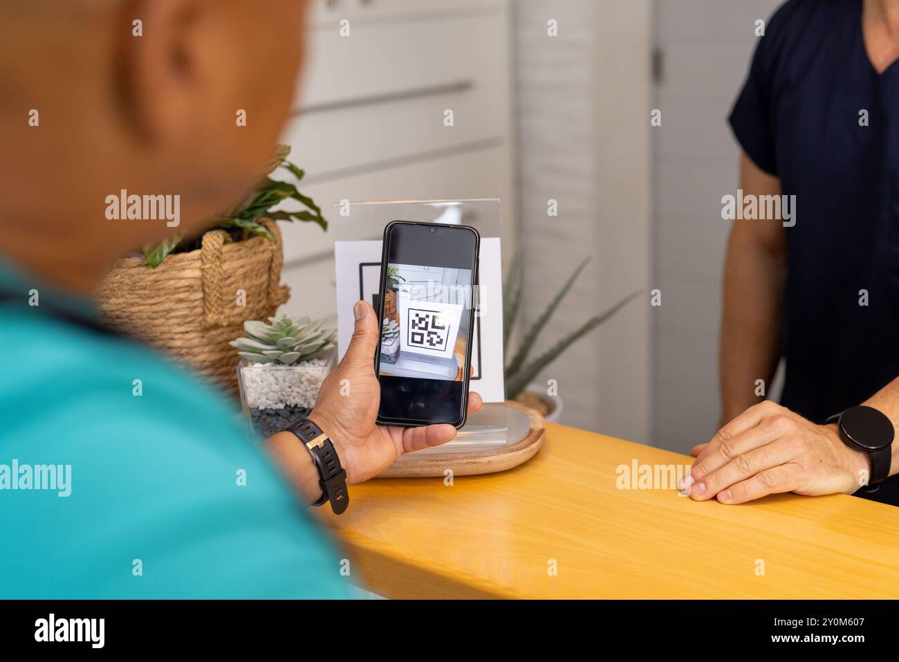Scanning QR code with smartphone, man at medical clinic reception desk ...