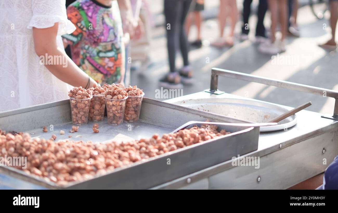 Close-up of caramelized nuts at a street food cart, with blurred people in the background.. Stock Photo