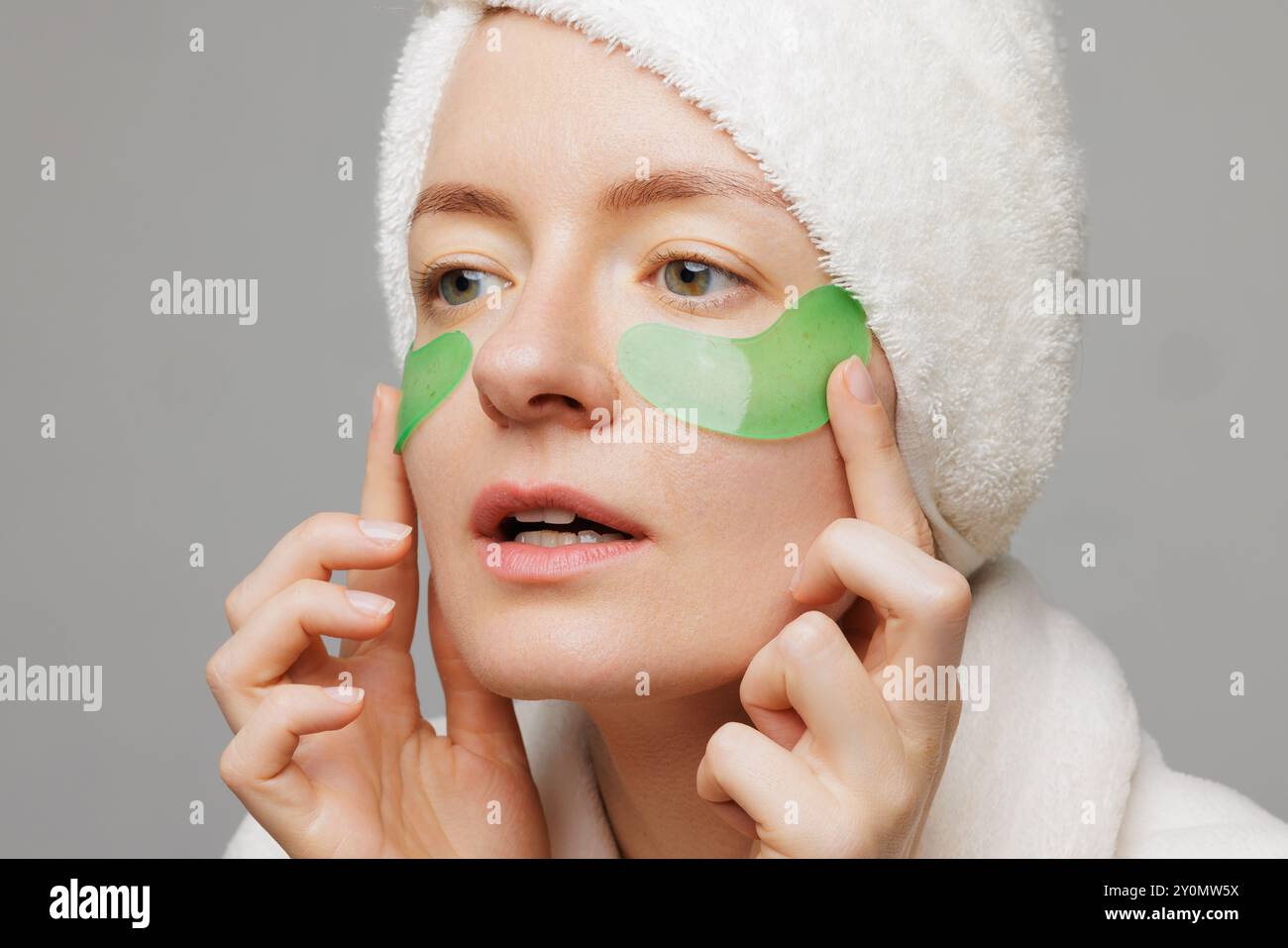A woman with a towel on her head and a robe smiles as she applies green ...