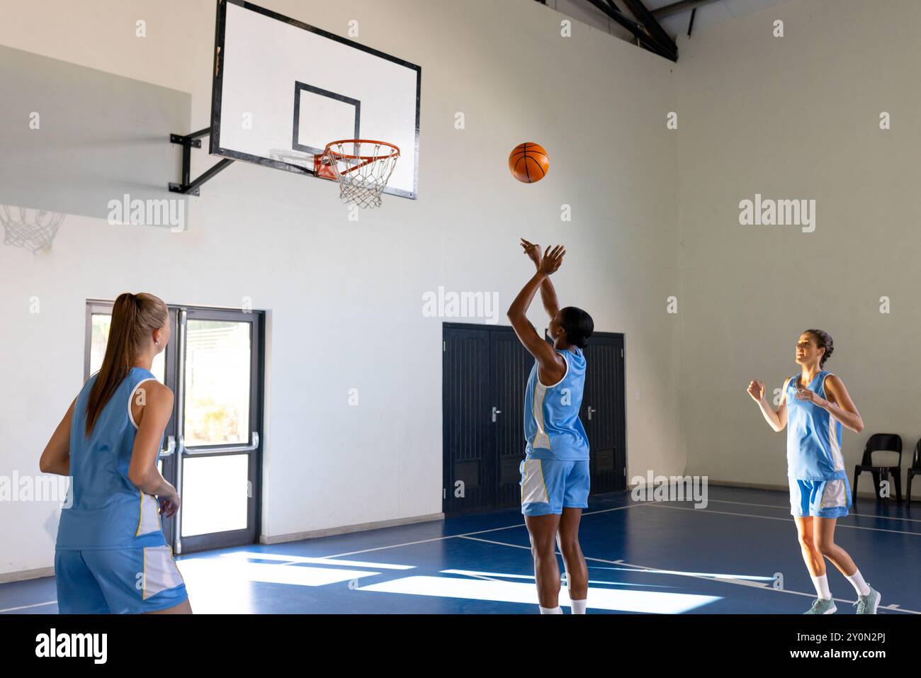 Playing basketball, female athletes practicing shooting on indoor school court Stock Photo