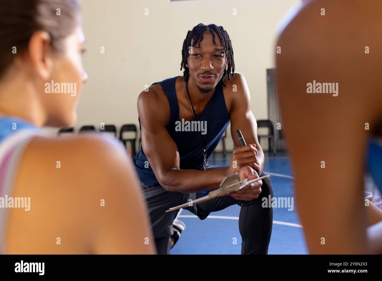 Male coach discussing strategy with female basketball players during practice session Stock Photo