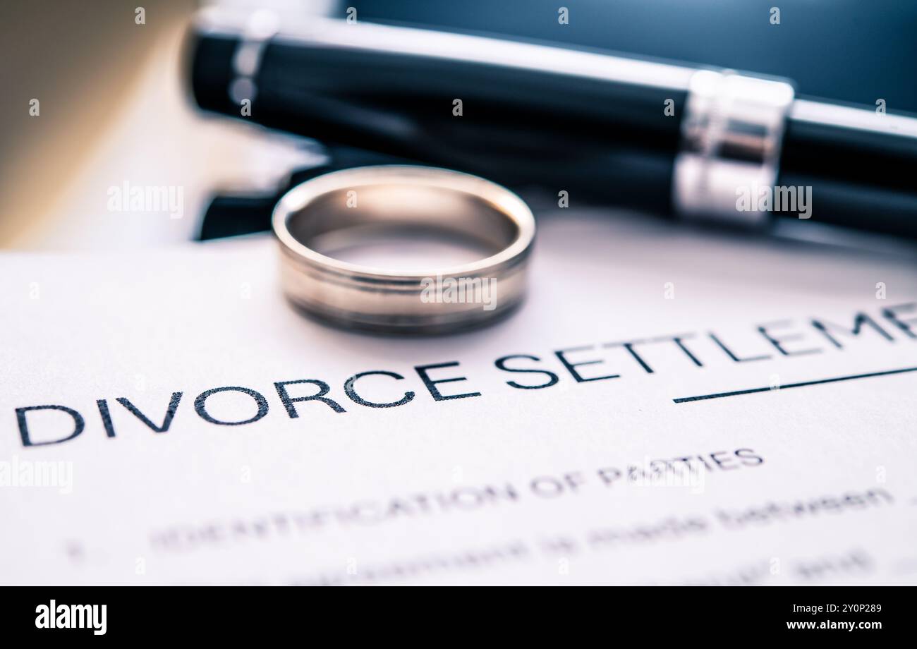 A divorce settlement agreement document with a wedding ring and pen placed on top, symbolizing the end of a marriage and the legal processes involved Stock Photo