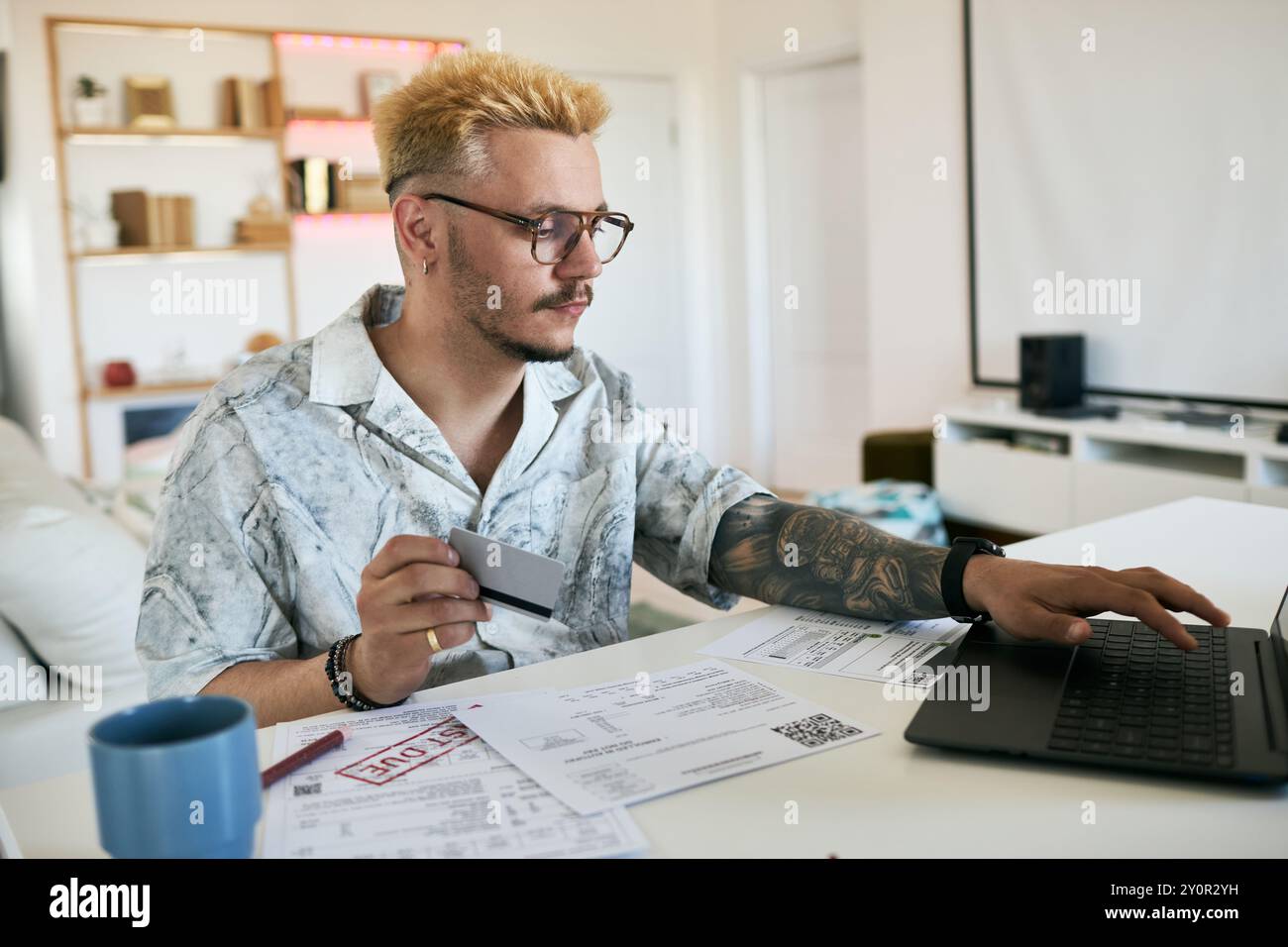 Focused young man analyzing documents and using laptop while working in modern home office setting Stock Photo