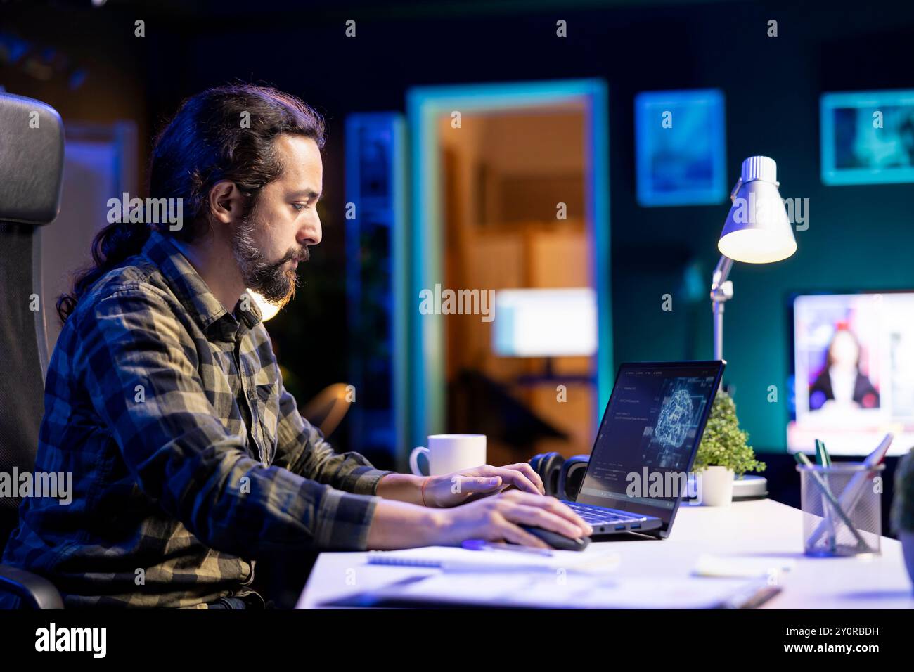Young man managing a complex system using machine learning on his portable computer. Focused male programmer sitting and typing in code for creating neural network database on laptop. Stock Photo