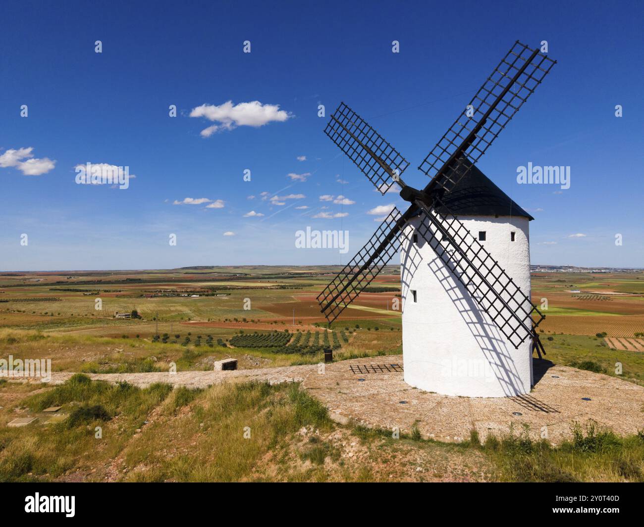 A single white windmill stands on a grassy field under a blue sky with ...