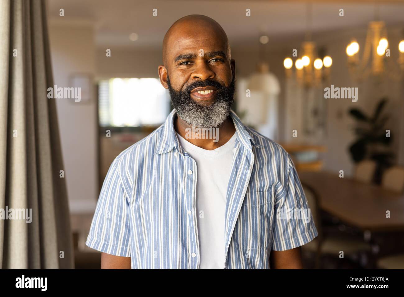 Smiling african american senior man in casual shirt standing in home, looking confident Stock Photo