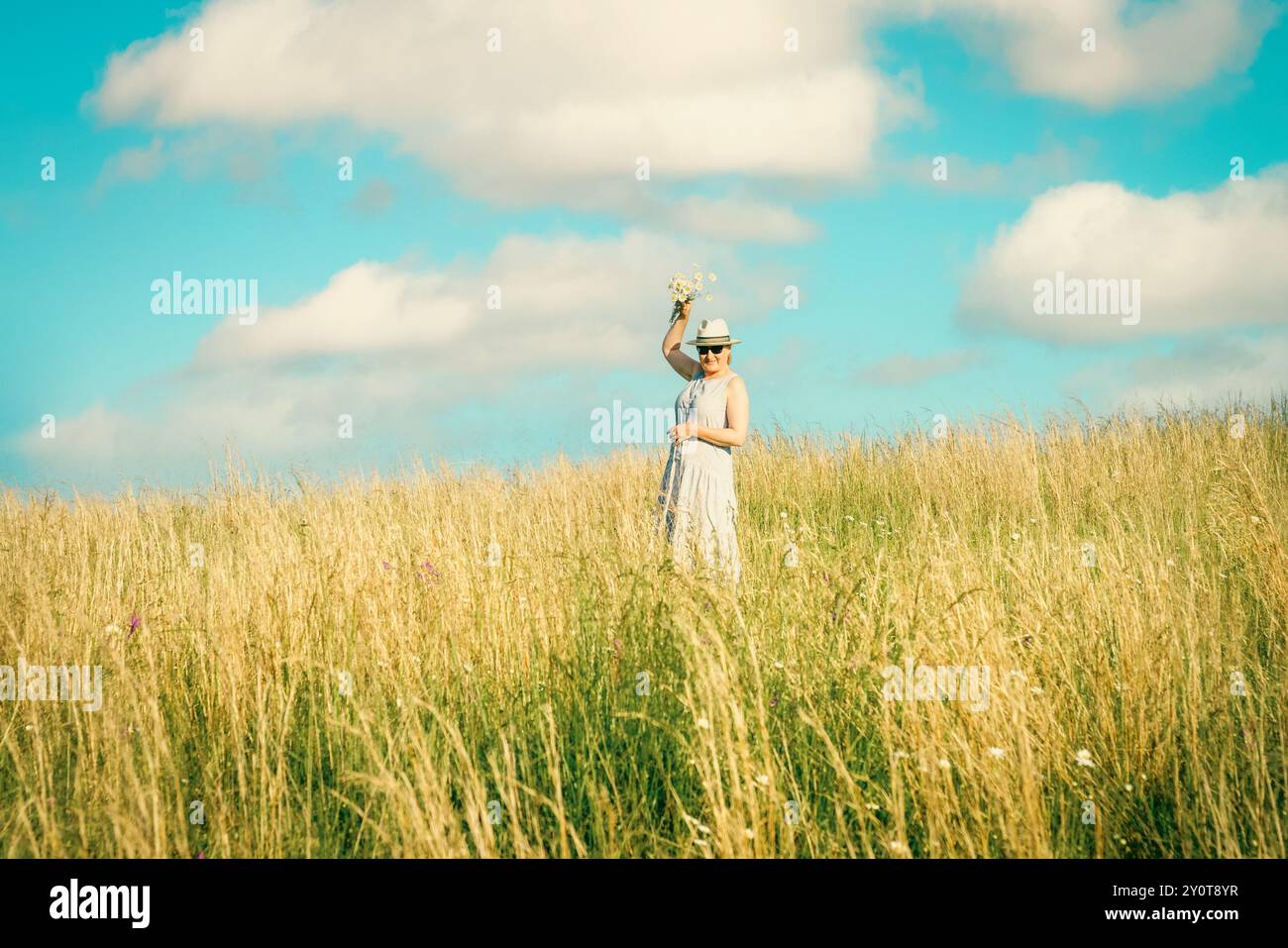 Happy mature woman with wildflowers in a tall grass field on a bright summer day. Stock Photo