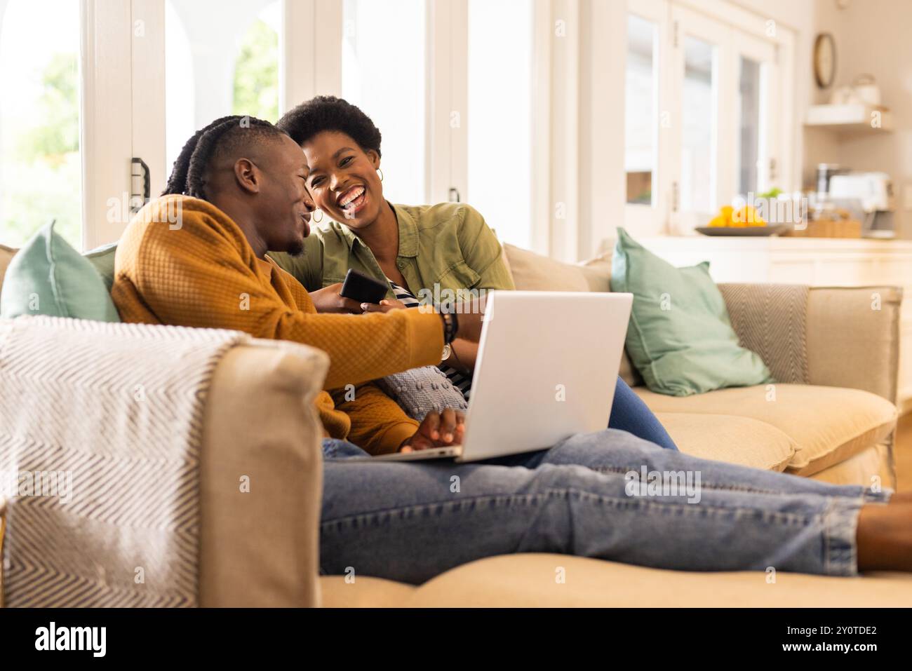 Relaxing on couch, African American couple using laptop and smartphone ...