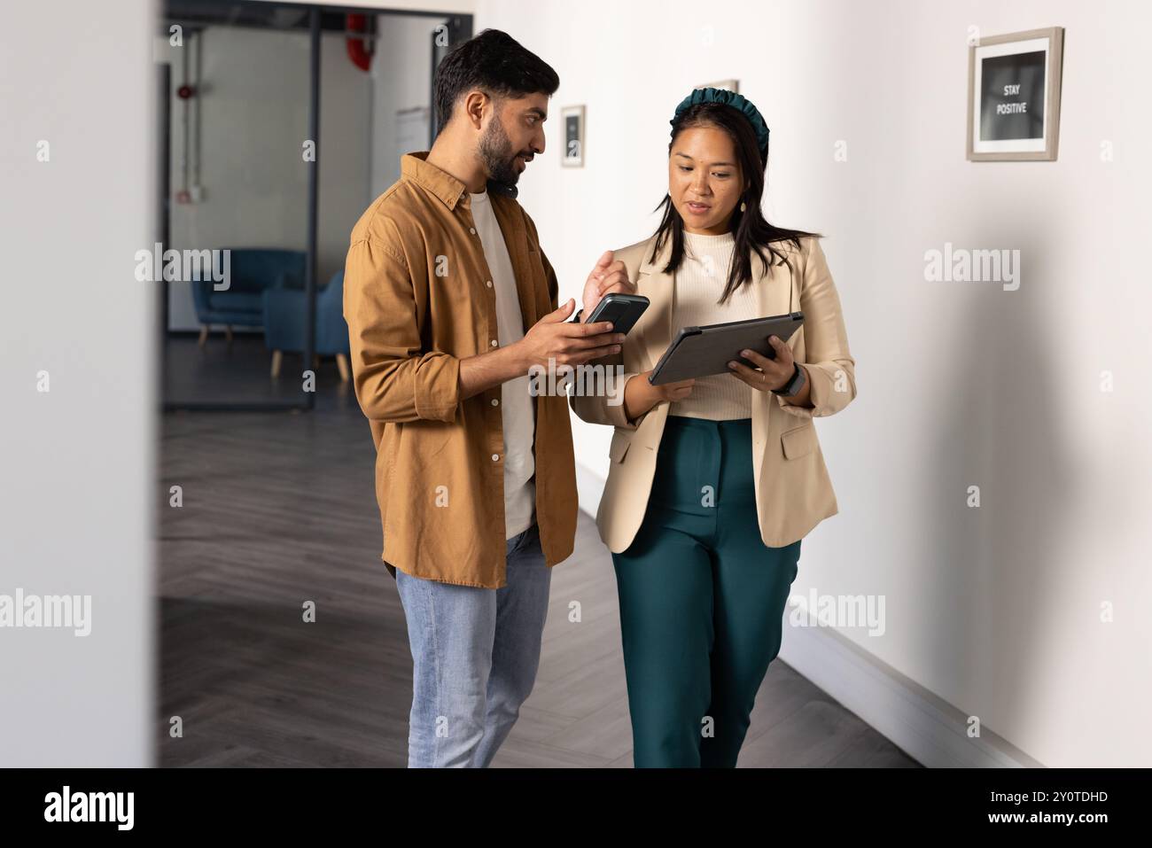Discussing work, colleagues using smartphone and tablet while walking in office Stock Photo