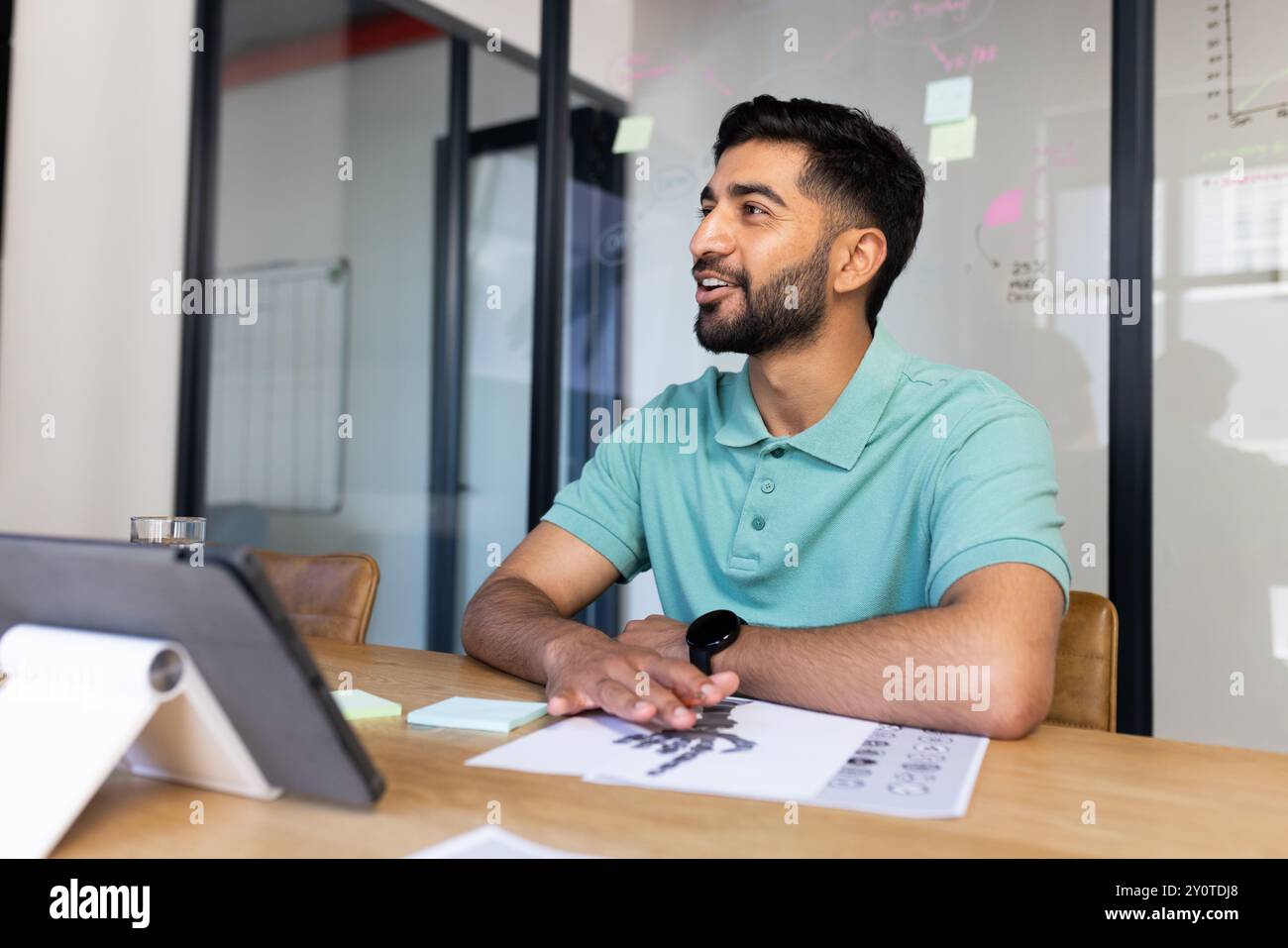Smiling Indian man in office discussing work, using tablet and documents on desk Stock Photo