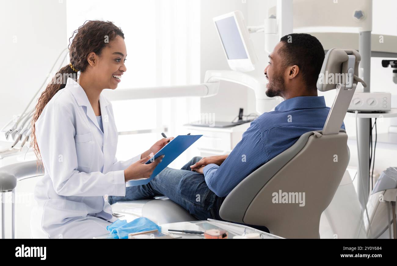 Smiling female dentist filling medical chart, talking to patient Stock Photo