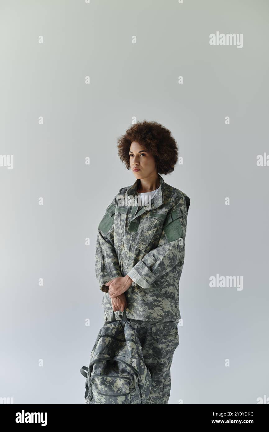 A confident young woman in camouflage, embodying strength and determination, stands ready for duty. Stock Photo