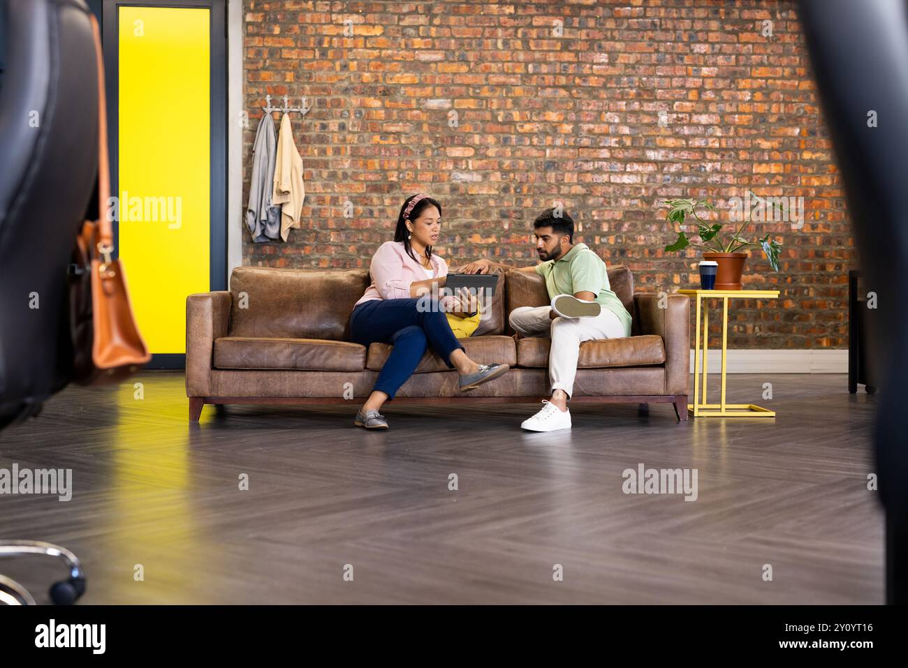 Collaborating on project, colleagues discussing ideas while using laptop on couch Stock Photo