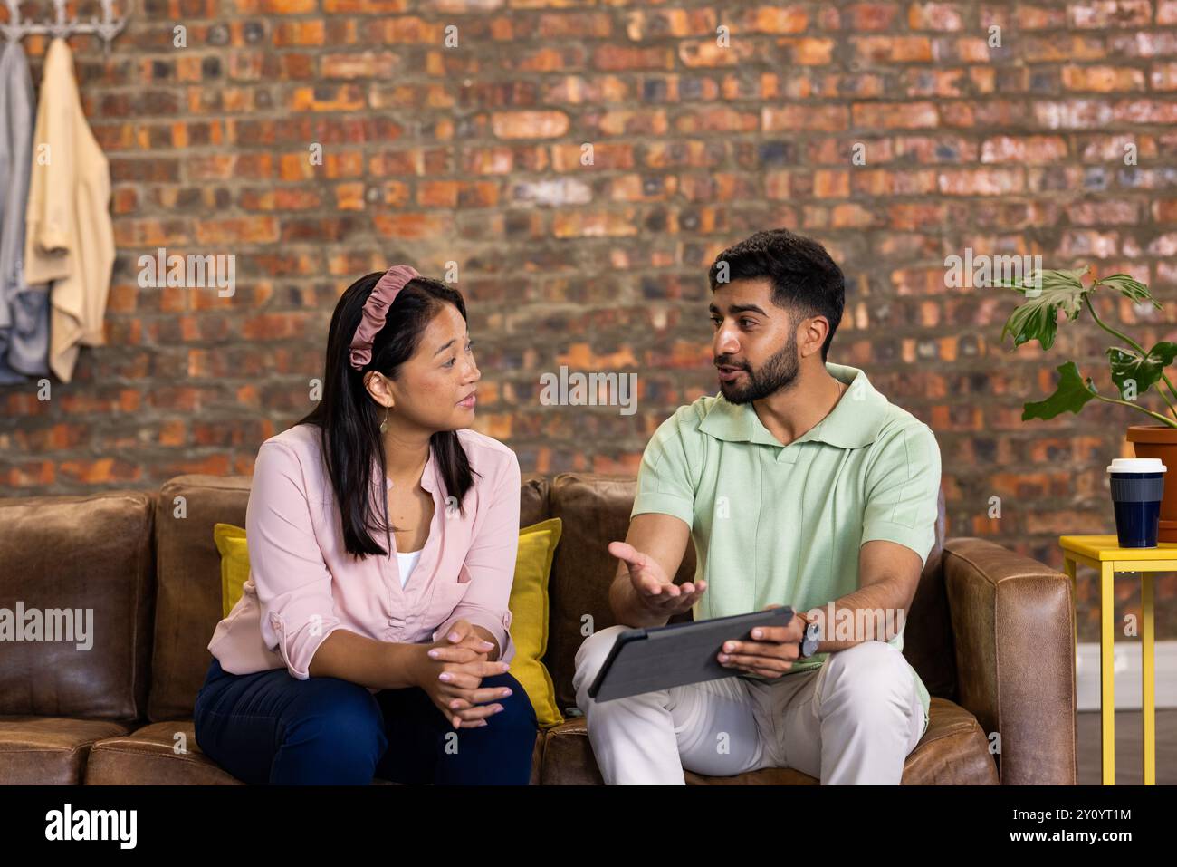 Discussing work, colleagues using digital tablet while sitting on office couch Stock Photo