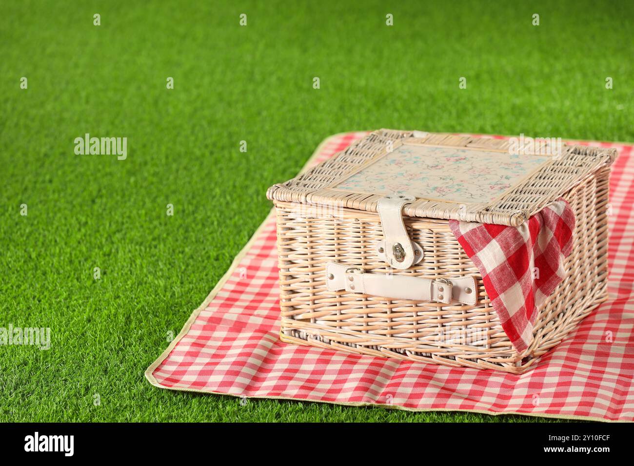 One picnic wicker basket with checkered napkin and blanket on green ...