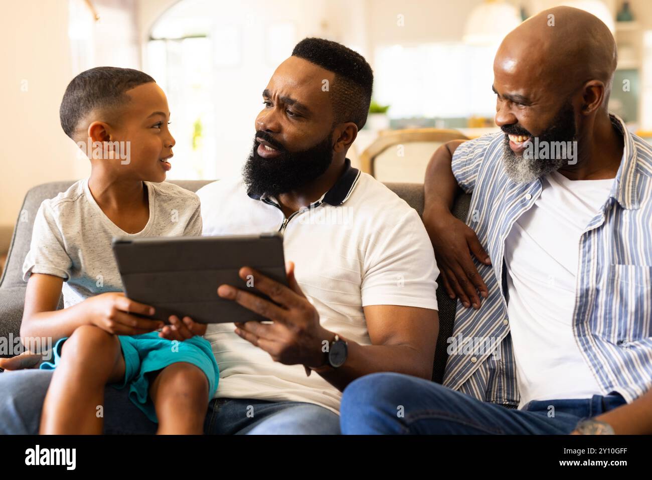 Using tablet, father and son sitting on couch with grandfather smiling Stock Photo