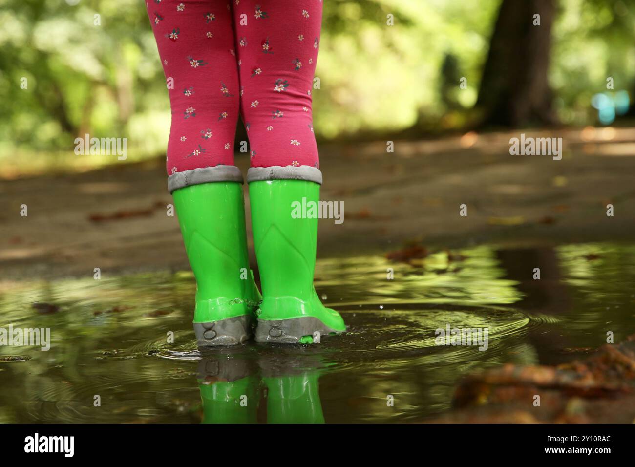 Little girl wearing green rubber boots standing in puddle outdoors ...