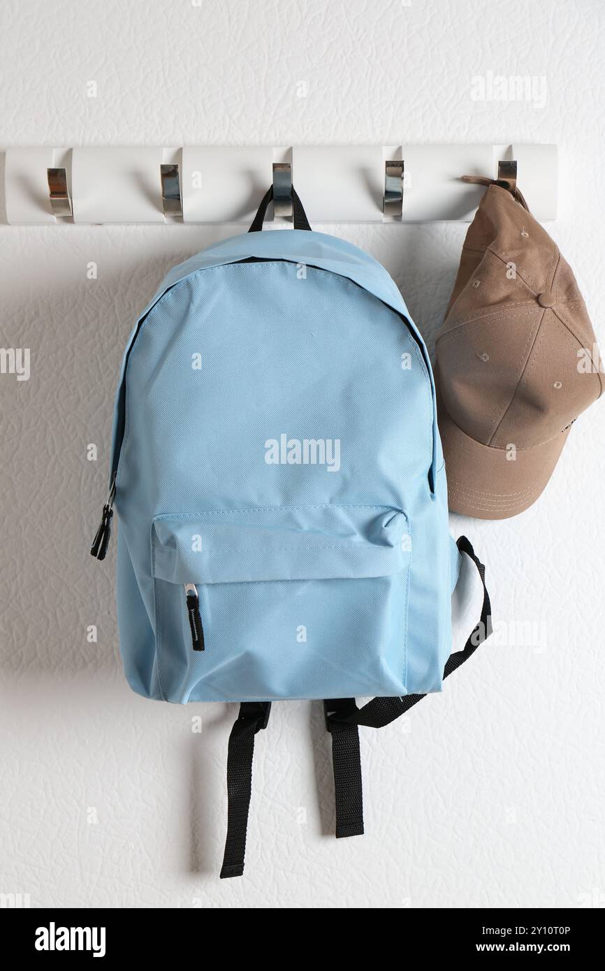 Light blue backpack and cap hanging on white wall Stock Photo