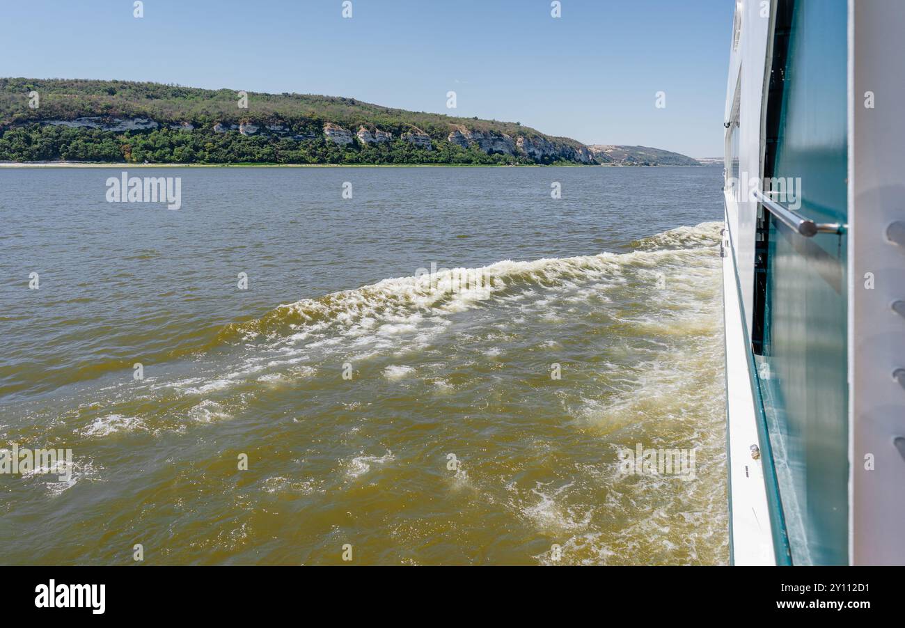 Picturesque river scene with limestone cliffs and lush vegetation, captured from boat with visible wake Stock Photo