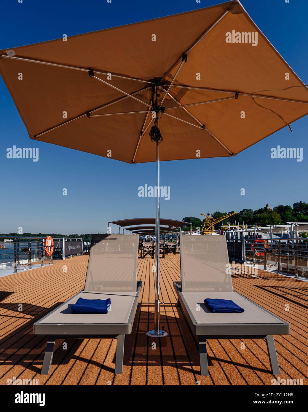 Two sun loungers under tan umbrella on boat deck with blue sky Stock Photo