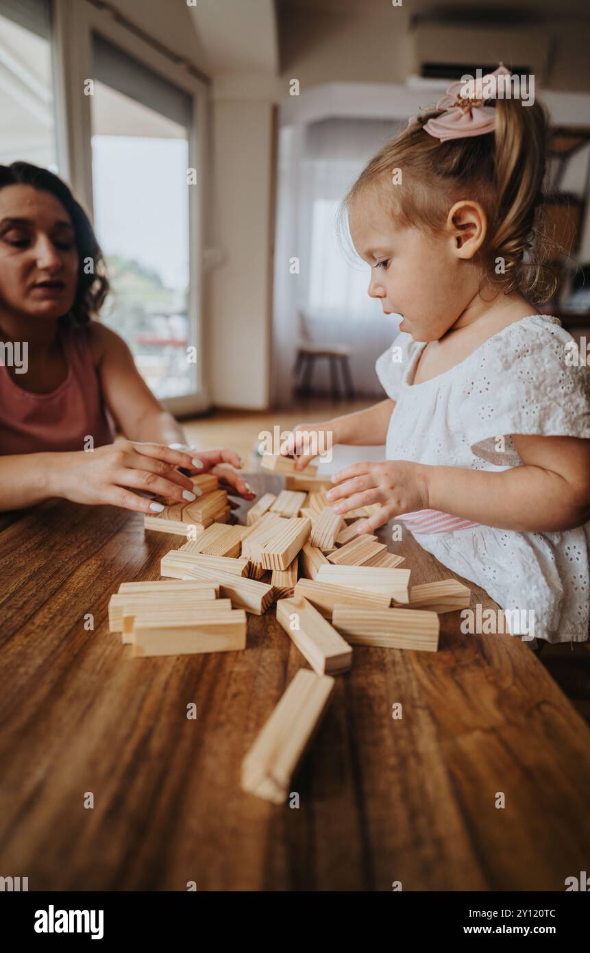 Mother and daughter playing with wooden blocks at home during a bonding ...