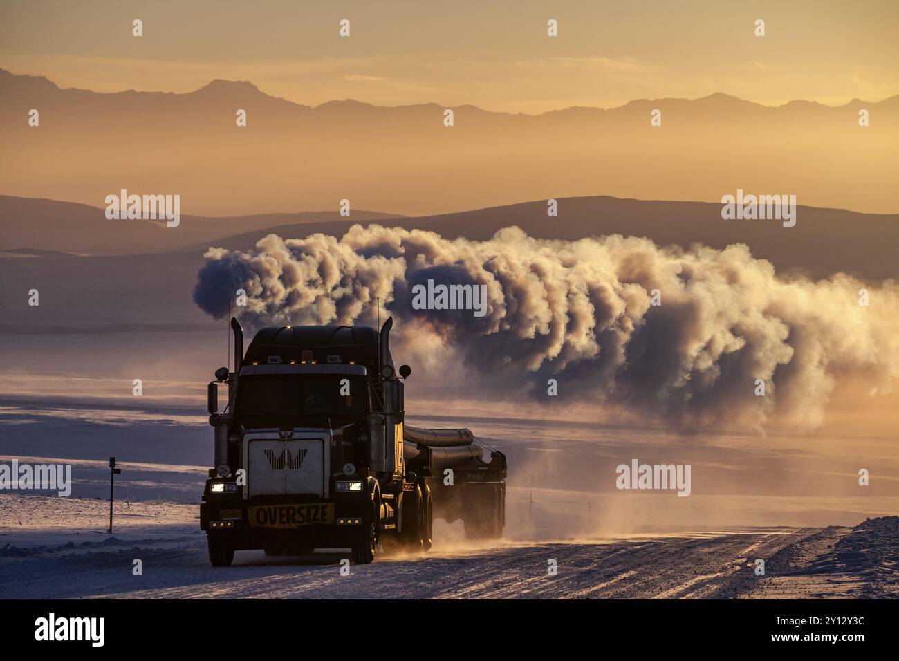 Truck on snowy track with large exhaust cloud in front of mountains in ...