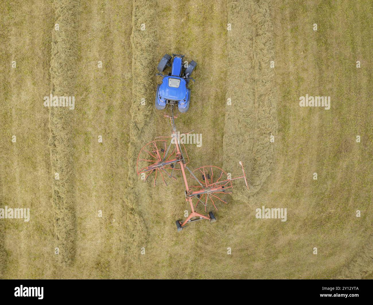 An aerial view shows a tractor with a hay tedder ploughing patterns ...
