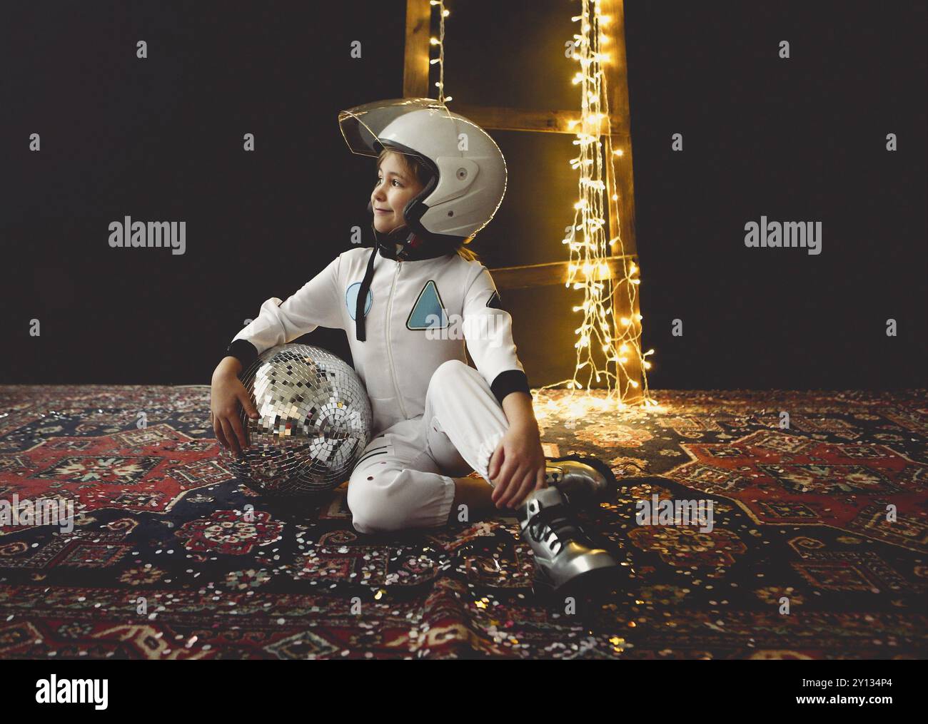 Astronaut futuristic kid girl with white full length uniform and helmet wearing silver shoes and holding disco ball Stock Photo