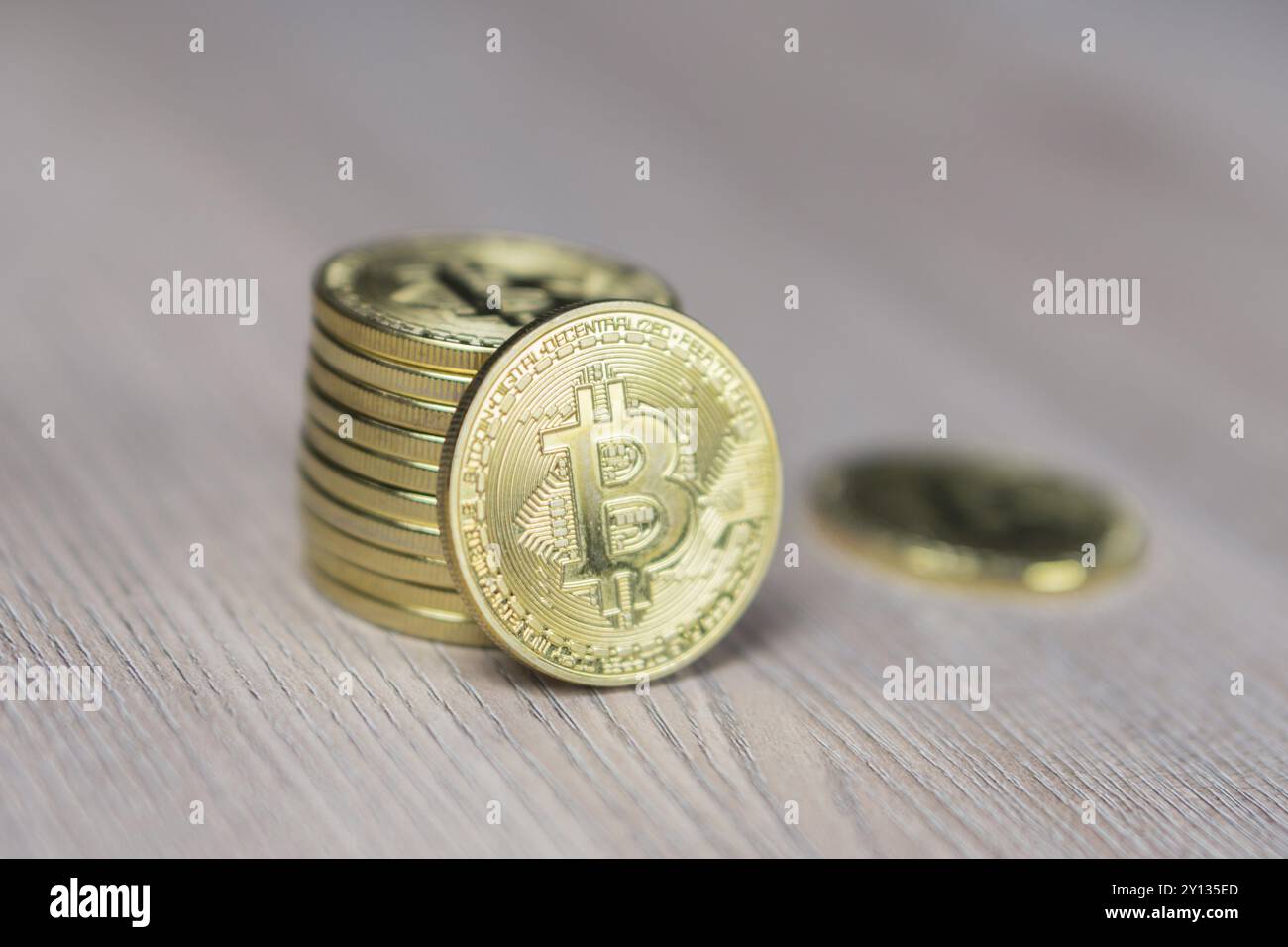 Stack of bitcoins with gold background with a single coin facing the camera in sharp focus with shading on the icon letter B on the face of the bit co Stock Photo