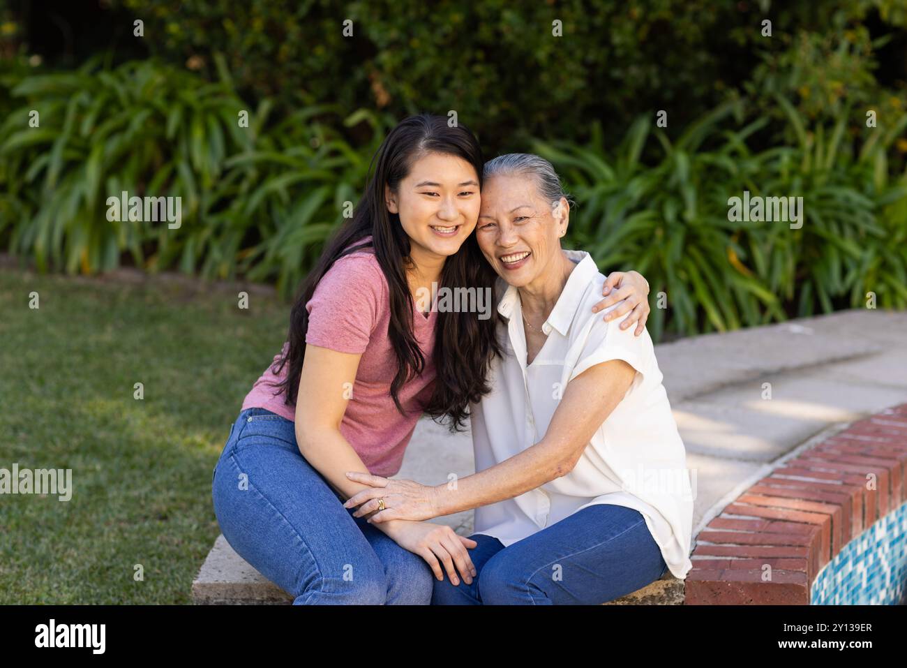 Smiling asian woman and asian grandmother sitting outdoors, hugging and enjoying time together Stock Photo