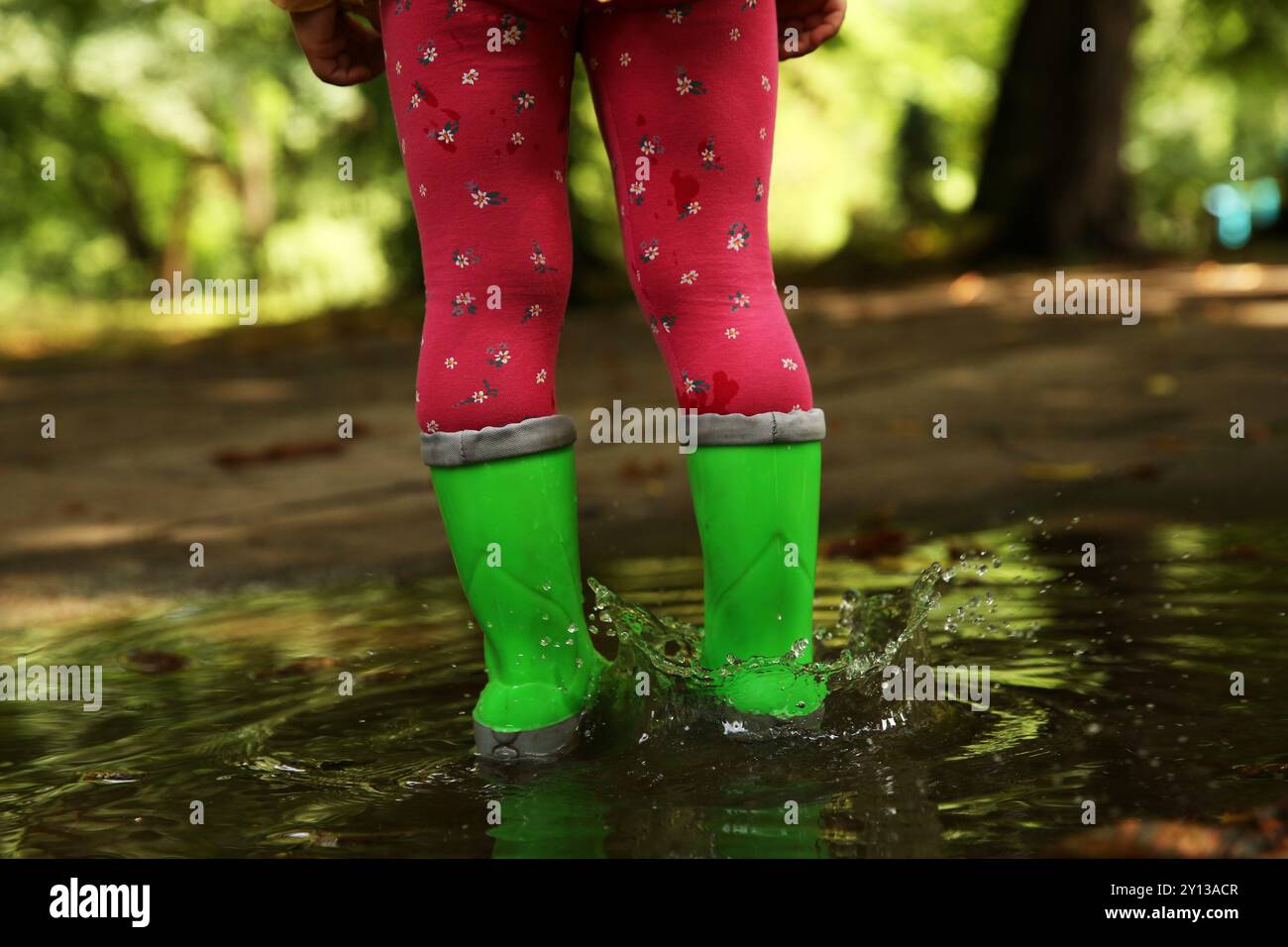 Little girl wearing green rubber boots standing in puddle outdoors ...